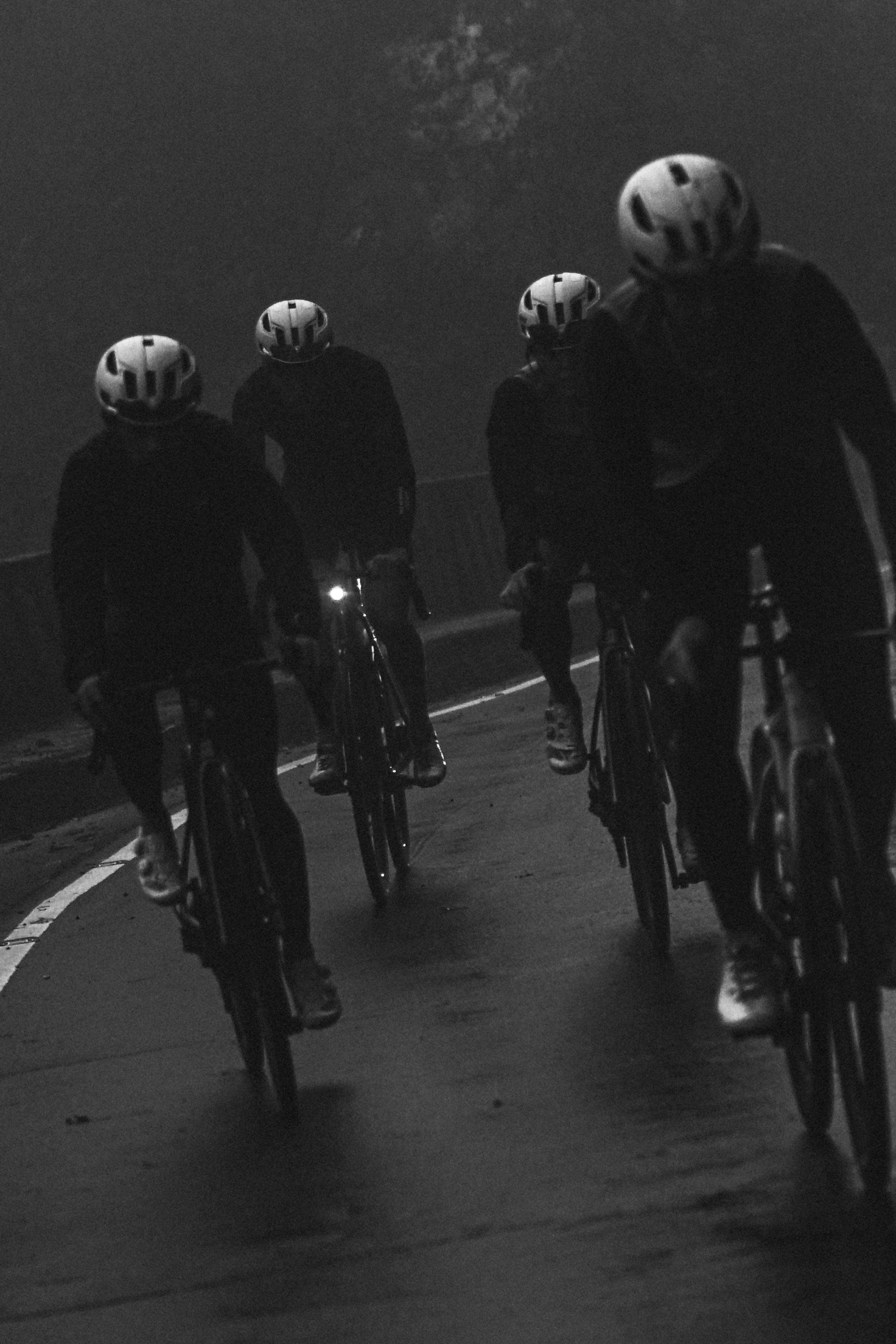 Four cyclists in dark cycling apparel and helmets riding at night with bike lights