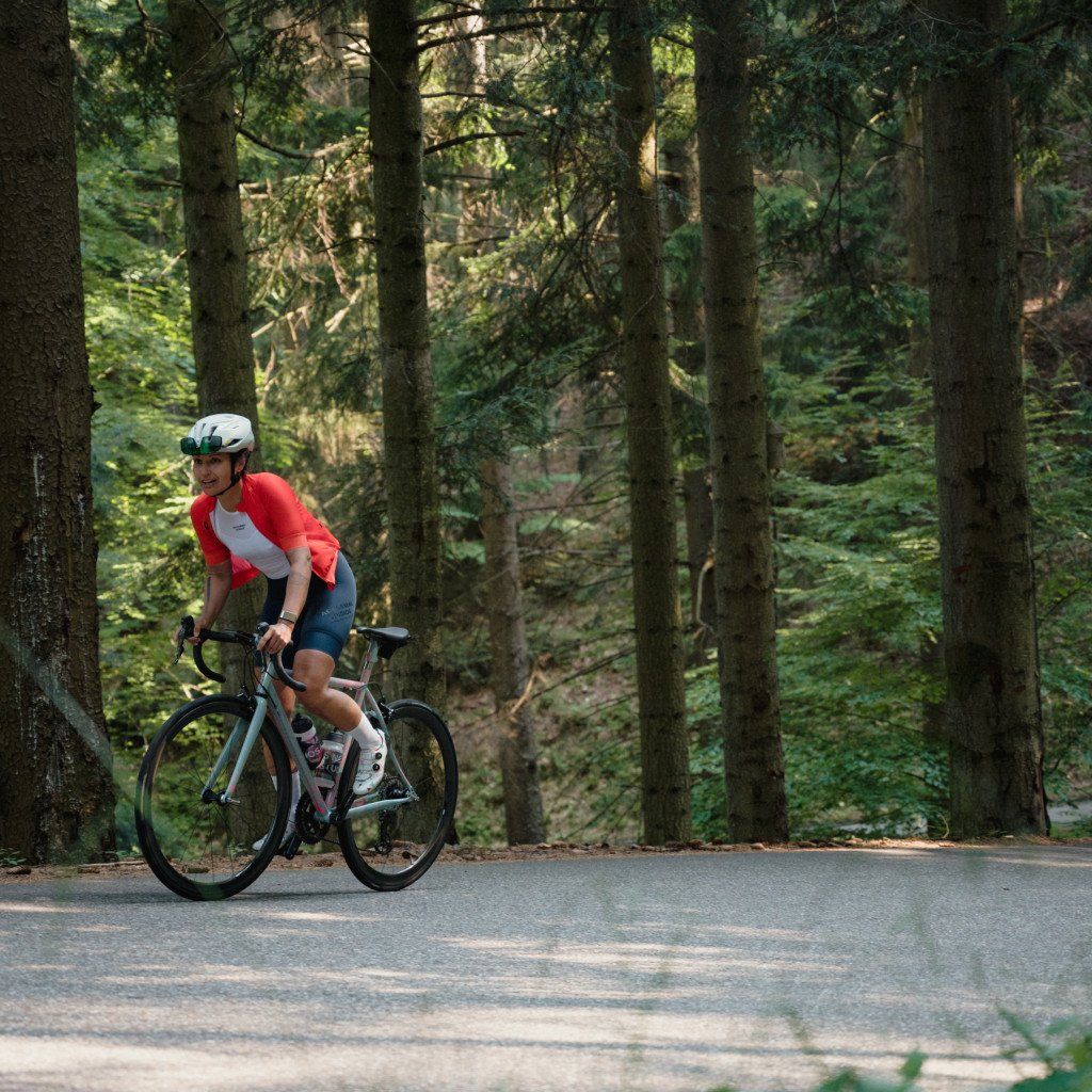 Model wearing red and white jersey with dark shorts cycling on forest road