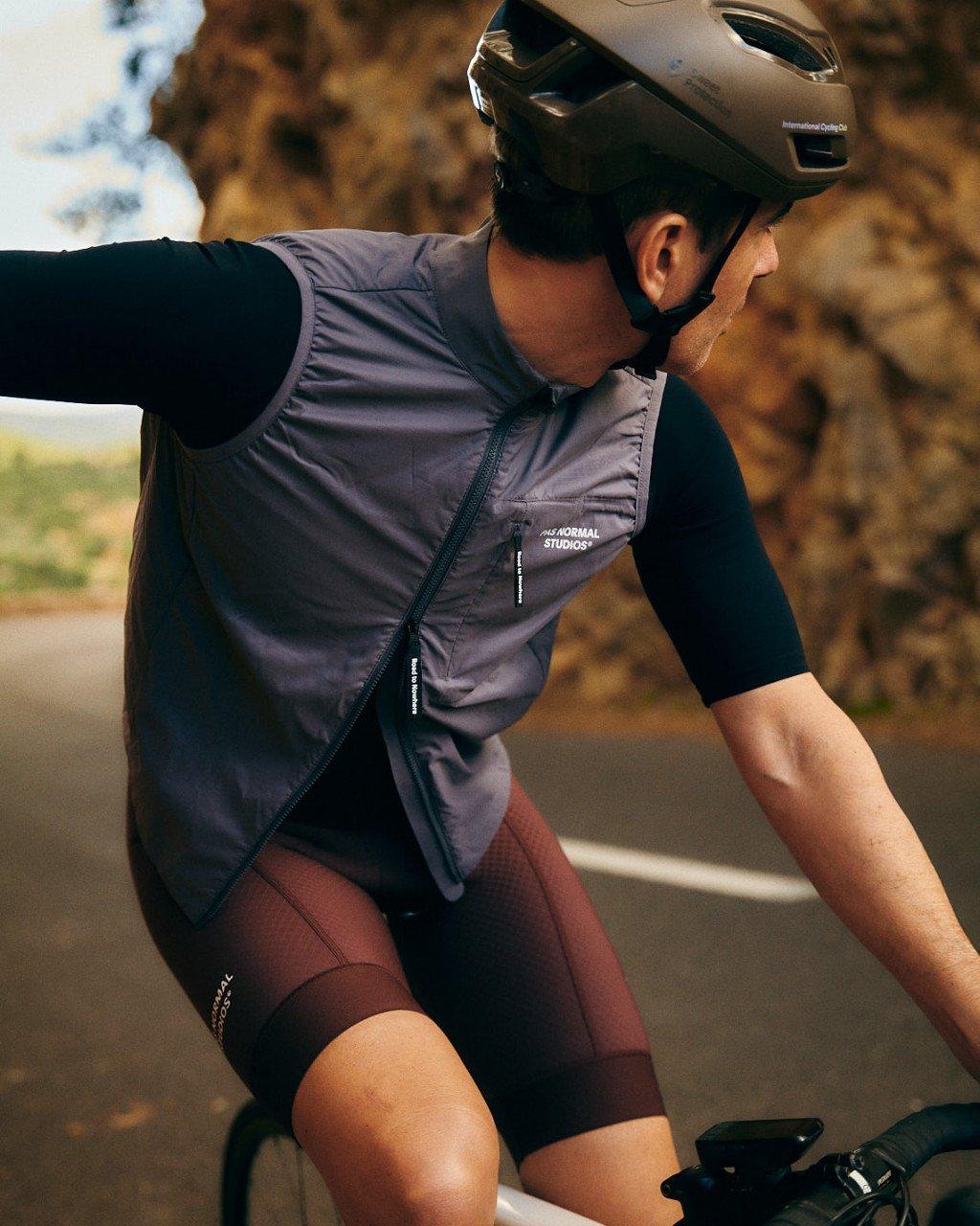 Model wearing grey cycling vest with black sleeves and shorts on road bike