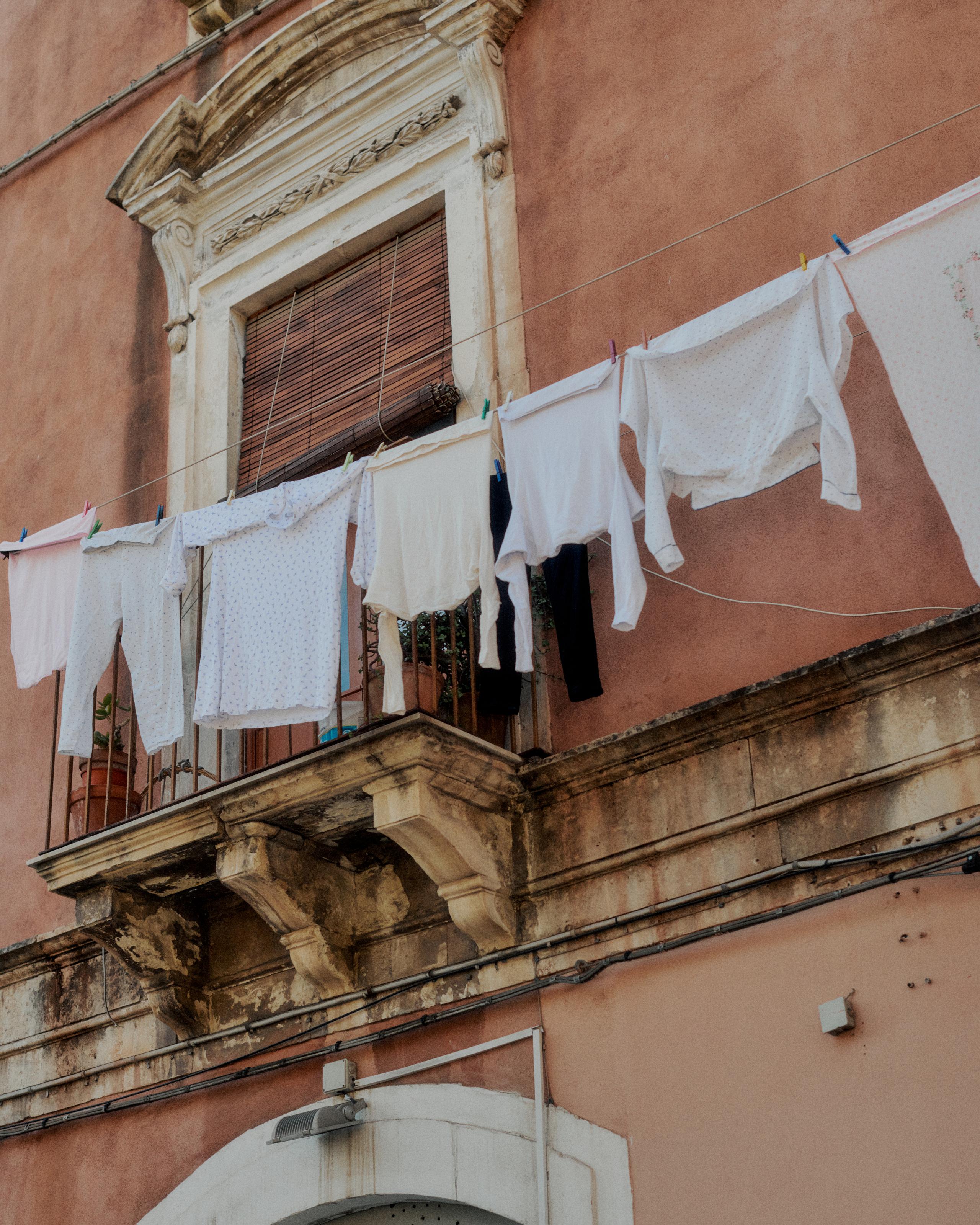 White laundry hanging on lines from ornate balcony of terracotta building in Sicily