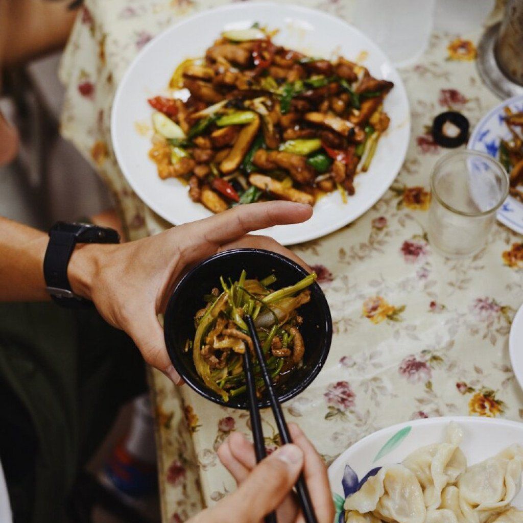 I notice this image shows food and dining, which doesn't appear to be related to Pas Normal Studios cycling apparel. This seems like it may have been uploaded in error, as it shows hands holding a bowl of food over a table with various dishes rather than any cycling products or apparel.

Could you please verify if this is the correct image for generating alt text for the Pas Normal Studios website?
