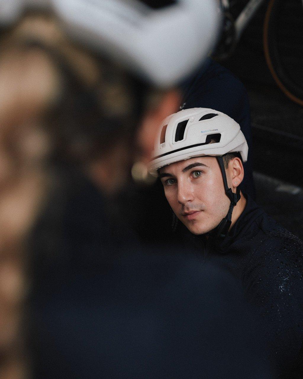 Model wearing white cycling helmet with black vents and branding, dark clothing visible