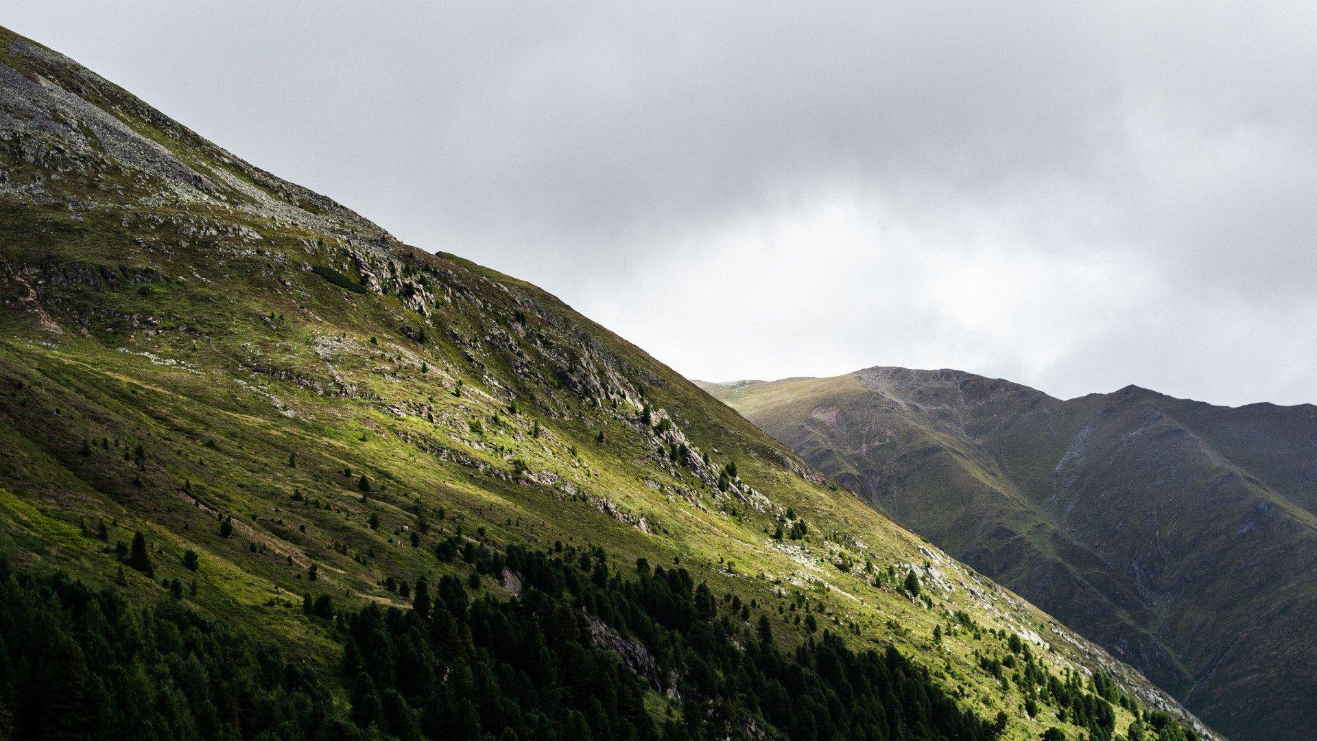 Green mountain landscape with rocky outcrops and valley under overcast sky