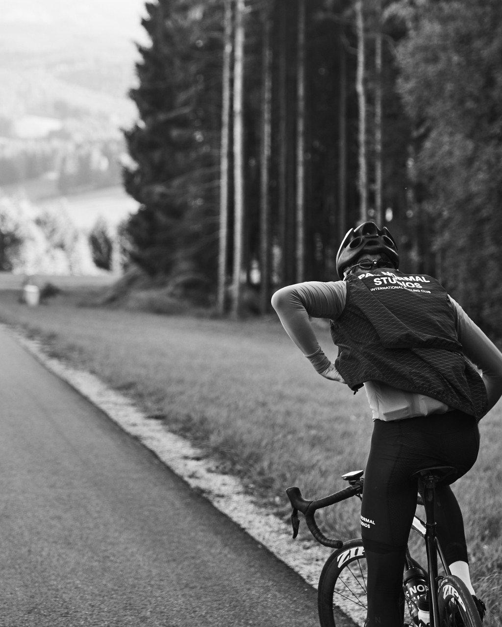 Model wearing cycling jersey with back logo cycling on tree-lined road, black and white photo