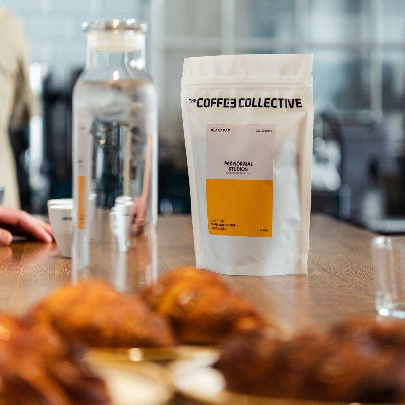 Coffee Collective white package with orange label on wooden table with brewing equipment and pastries
