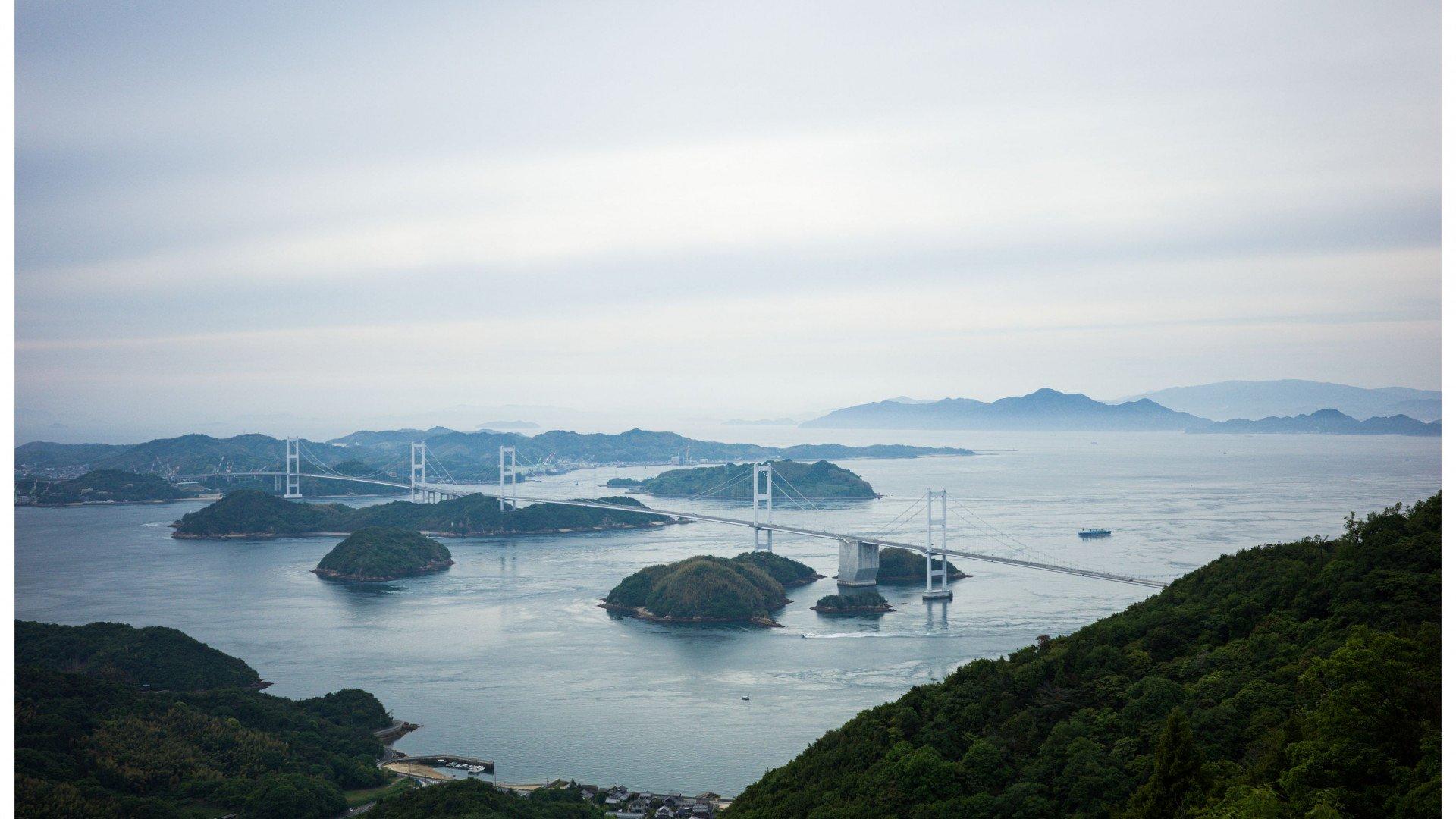Aerial view of suspension bridges connecting forested islands across calm blue waters in Japan