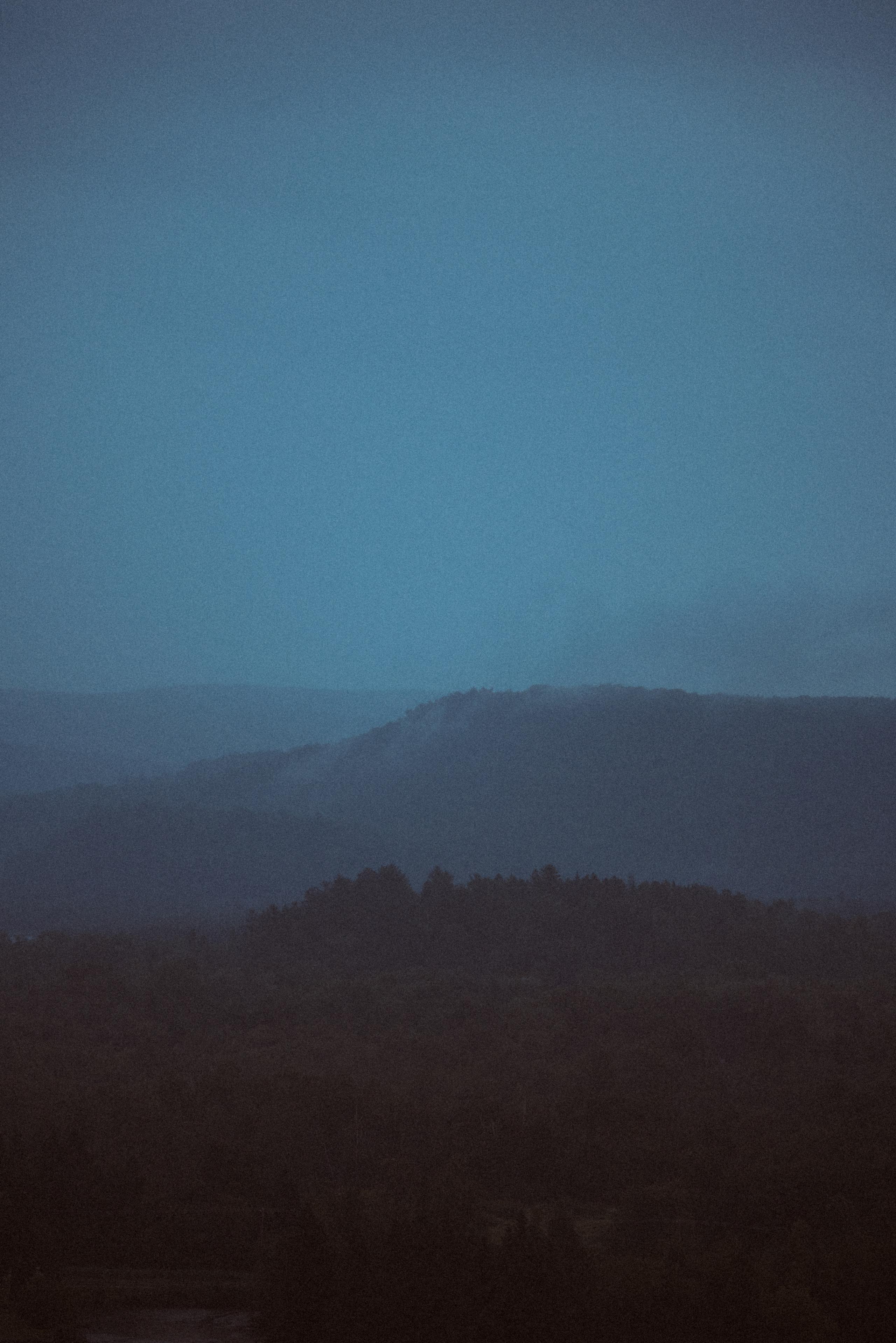 Misty blue mountain landscape at dawn or dusk with layered hills silhouetted against gradient sky
