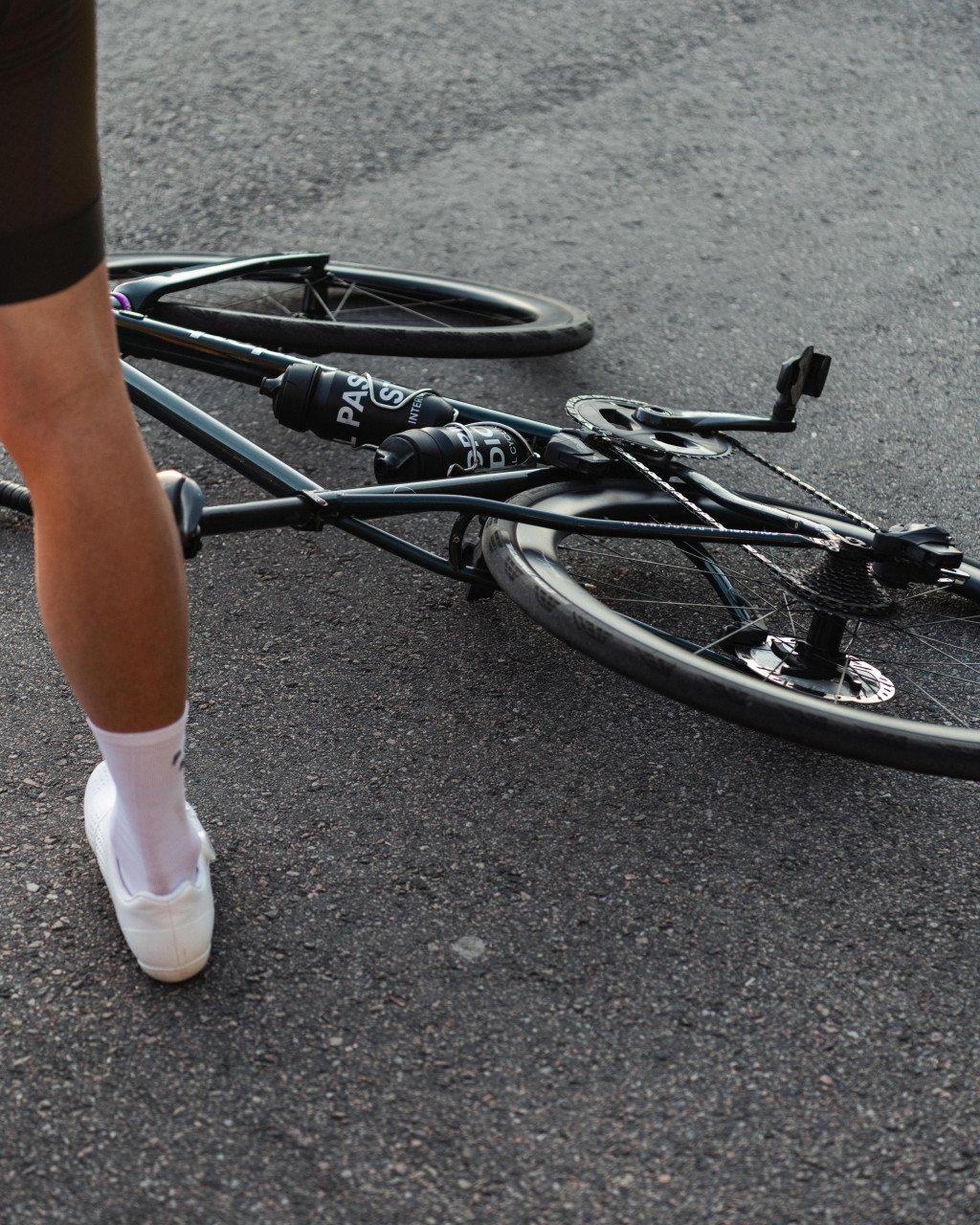 Cyclist's leg in white socks and shoes next to fallen bicycle on asphalt road