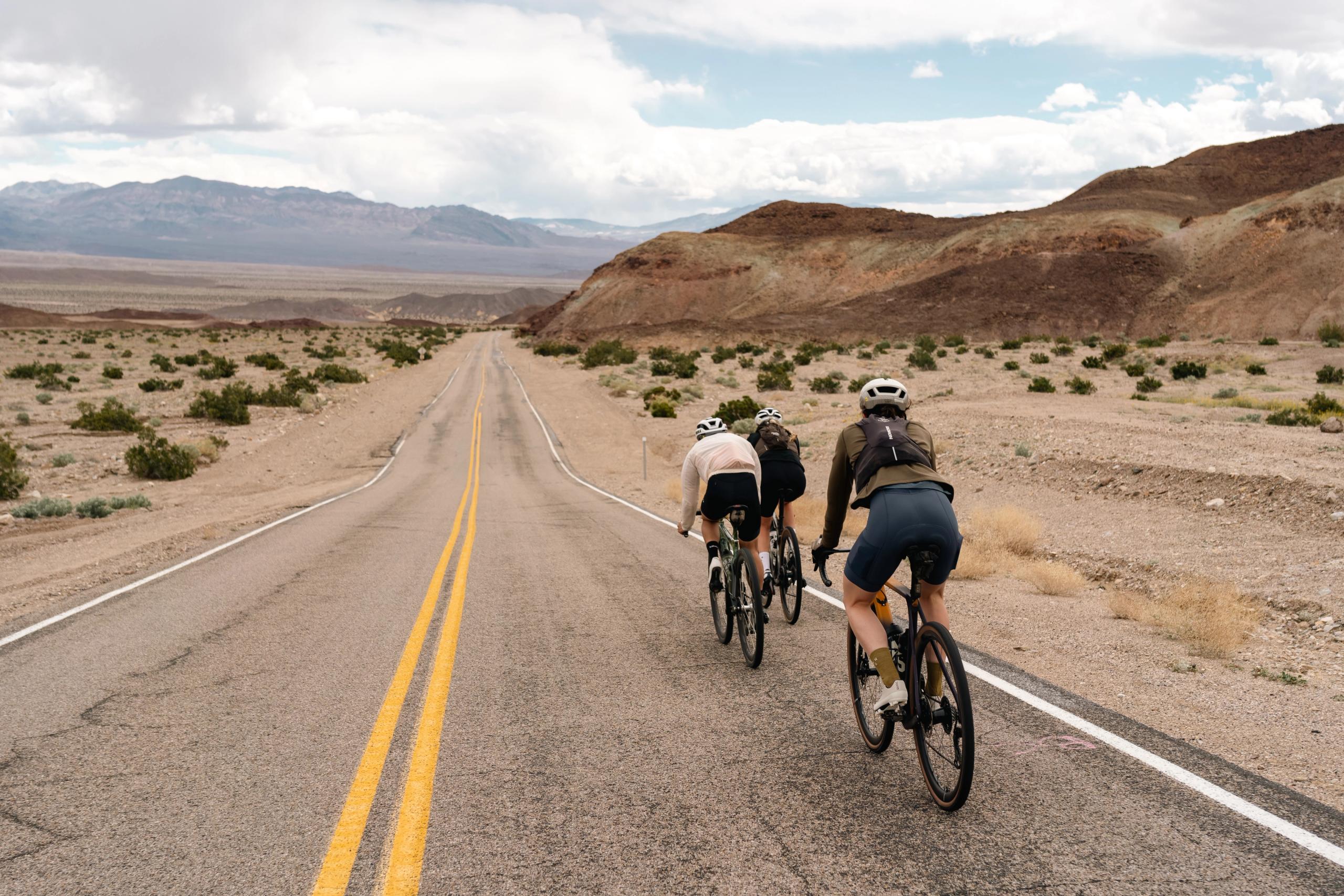 Cyclists riding in formation on desert highway through Death Valley landscape