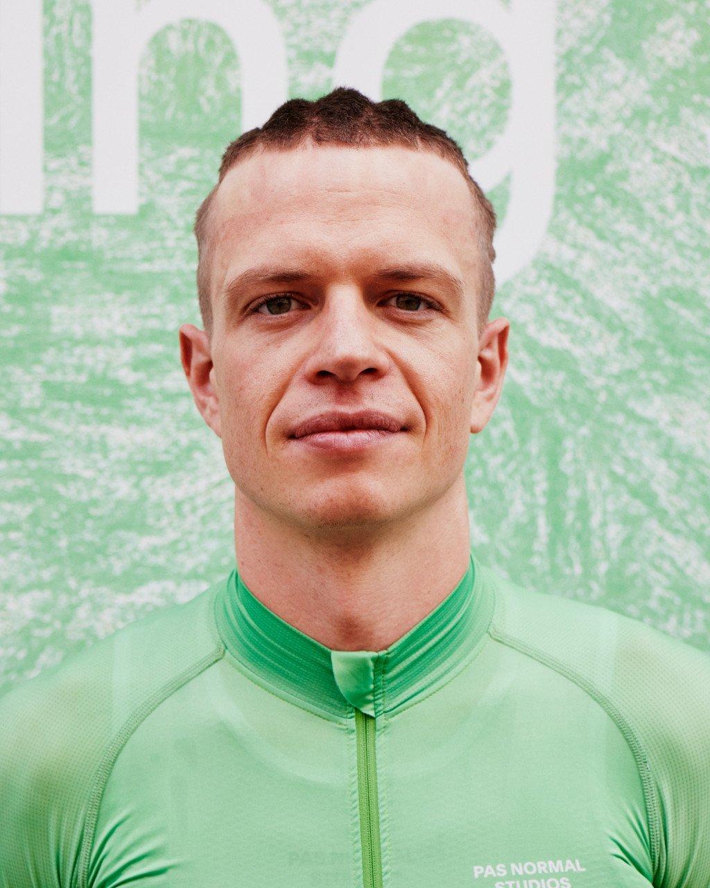 Model wearing green cycling jersey with full zip and high collar against green patterned background
