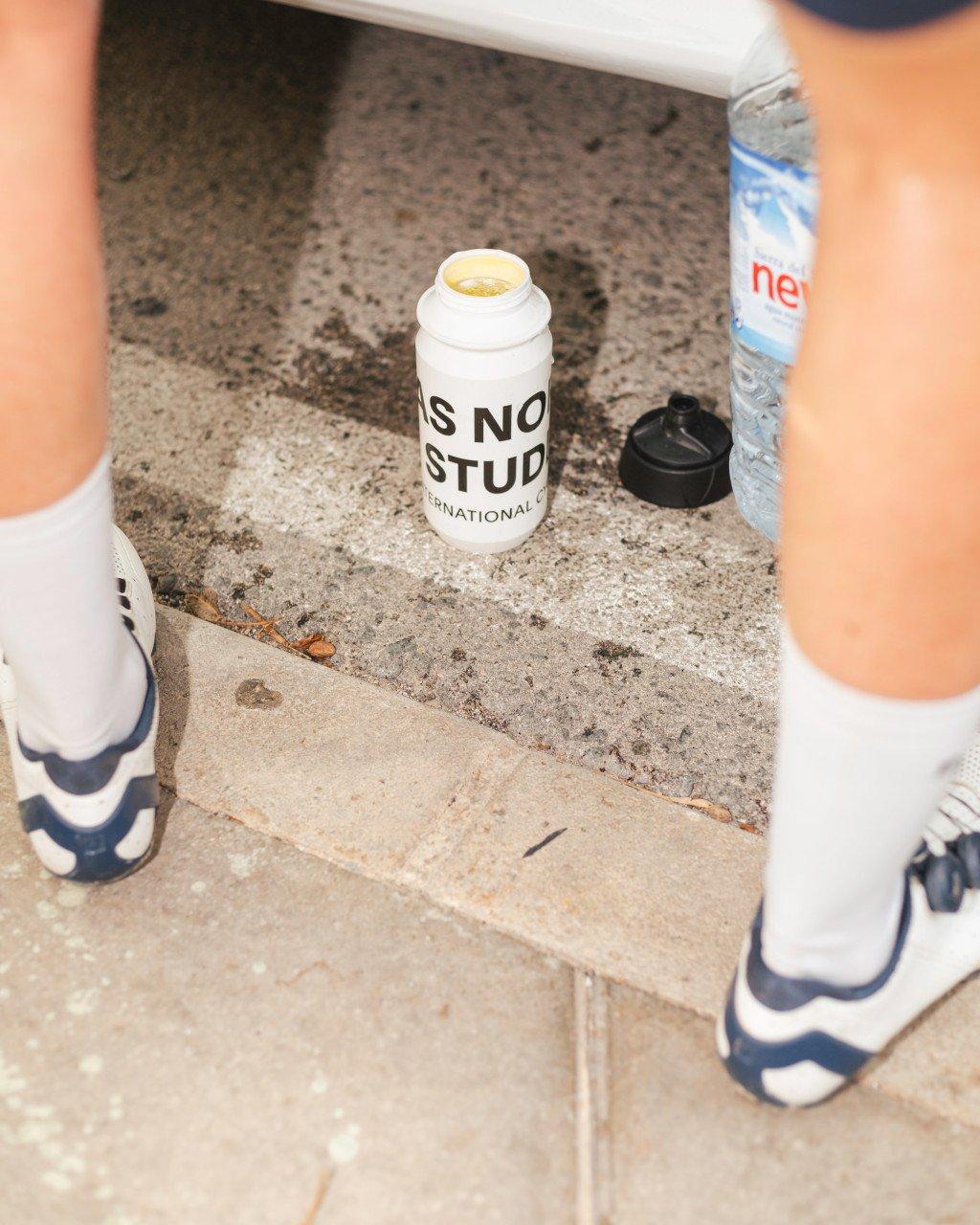 White branded water bottle on concrete steps with cycling shoes and water bottle