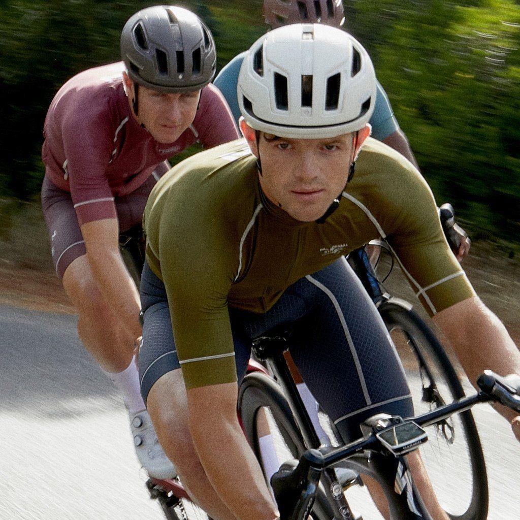 Models wearing cycling gear including olive green and burgundy jerseys with matching shorts on road