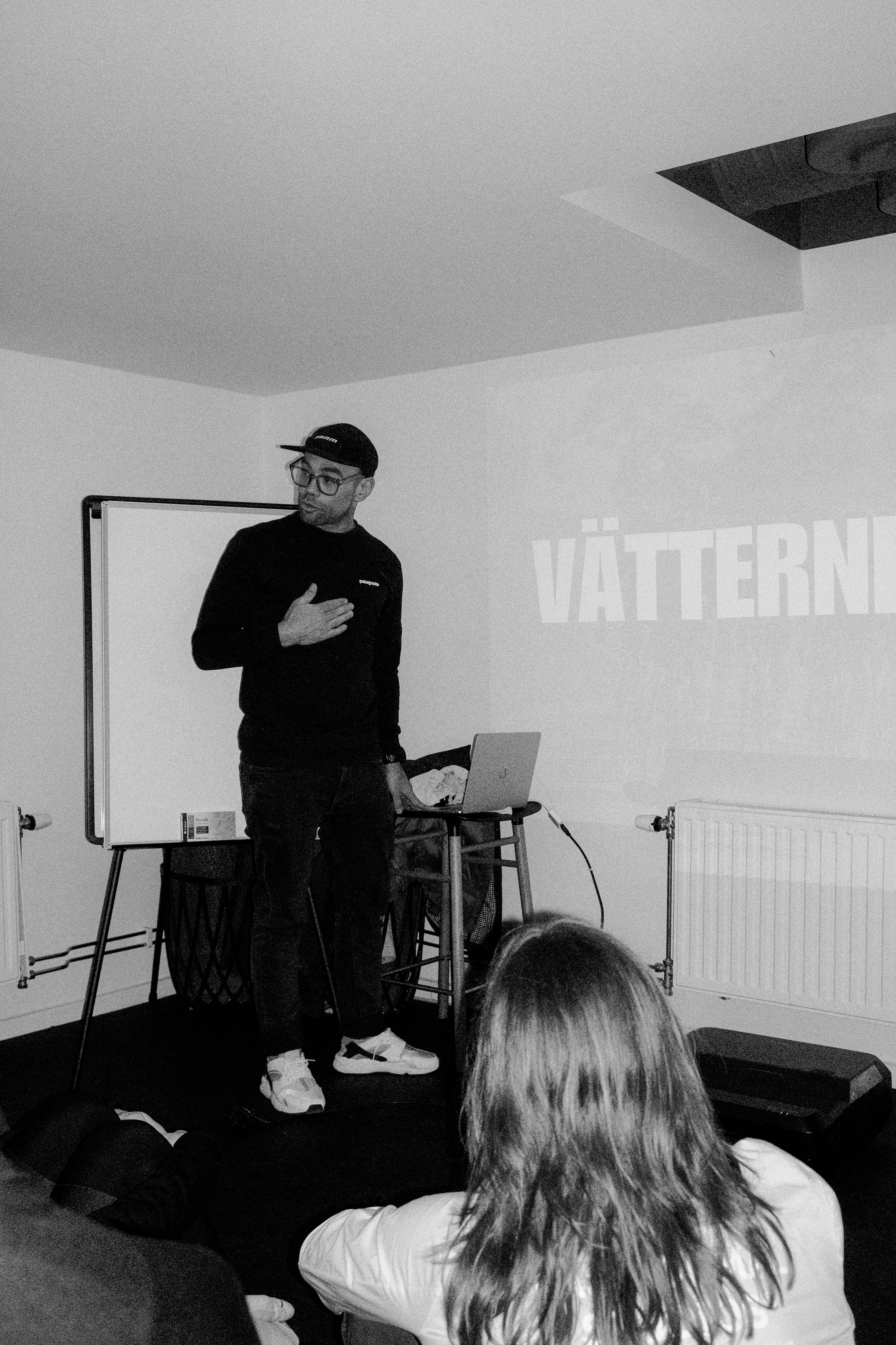 Man presenting in black long sleeve top and cap at cycling event discussion