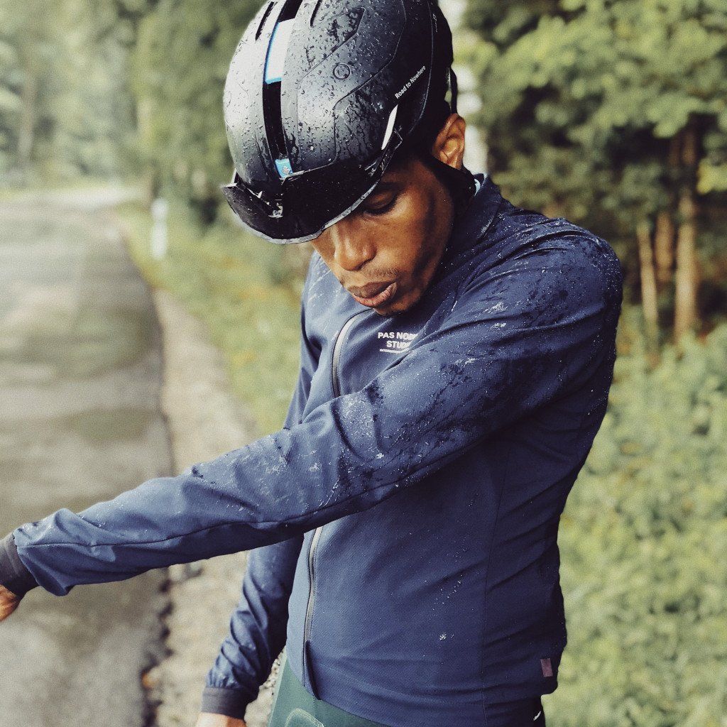 Model wearing blue cycling jacket with water droplets and helmet in outdoor setting
