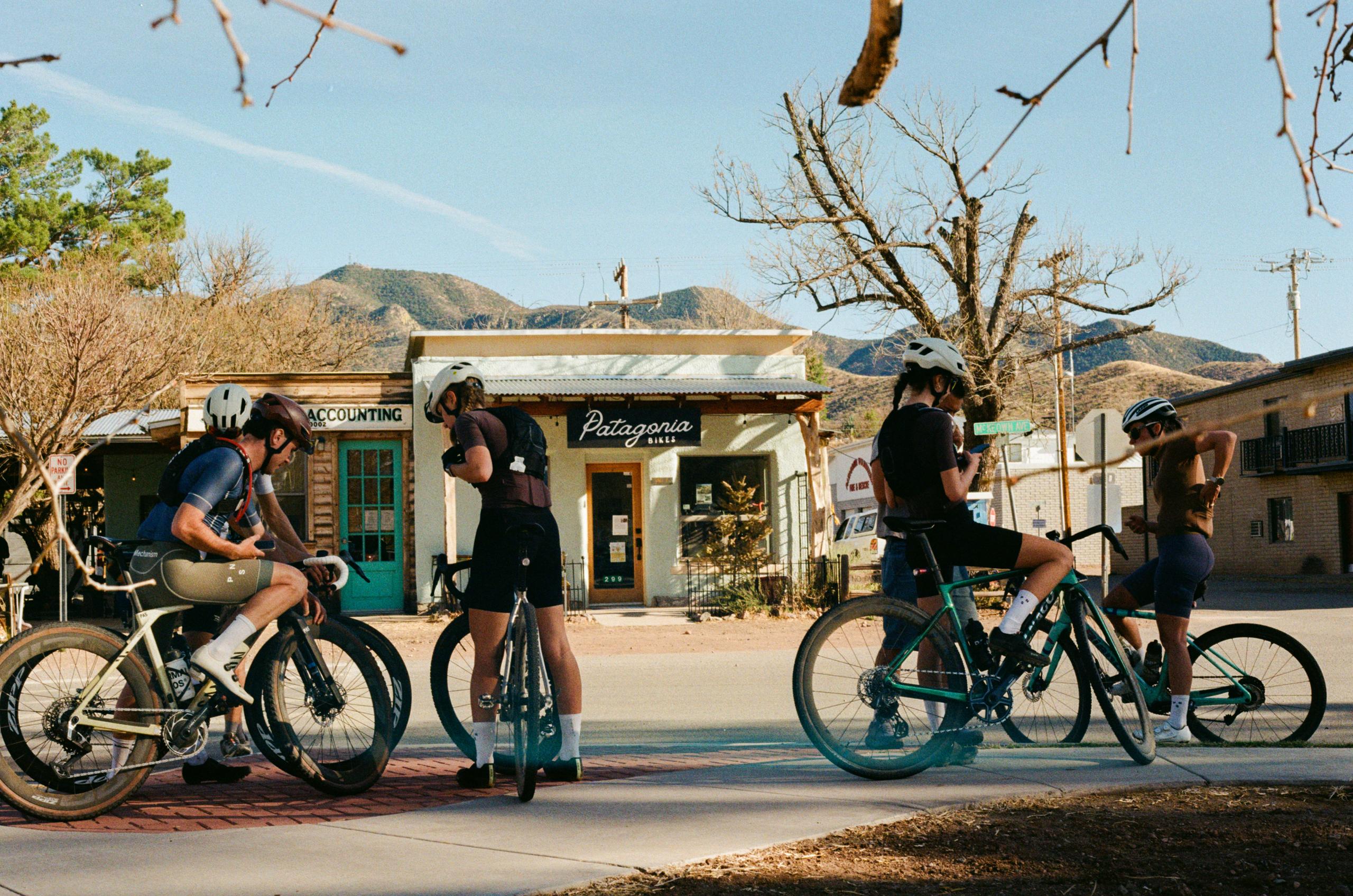 Group of cyclists in racing gear taking a break in small desert town with mountains in background