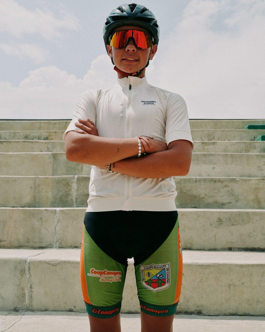 Model wearing white cycling jersey with arms crossed, wearing helmet and sunglasses