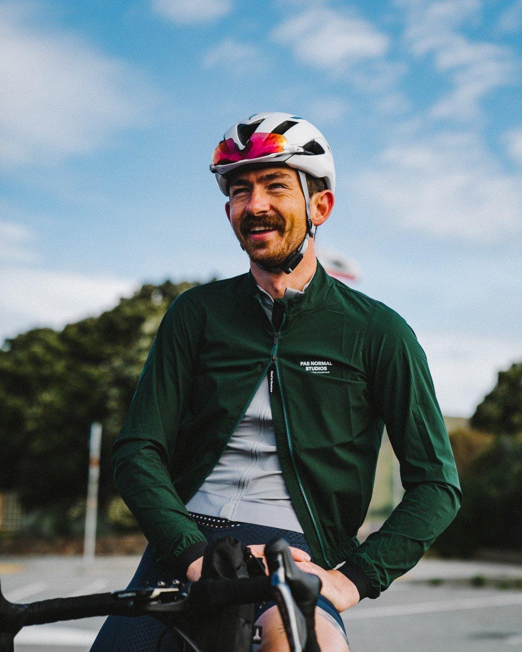 Model wearing green cycling jacket with white helmet, smiling outdoors with bike