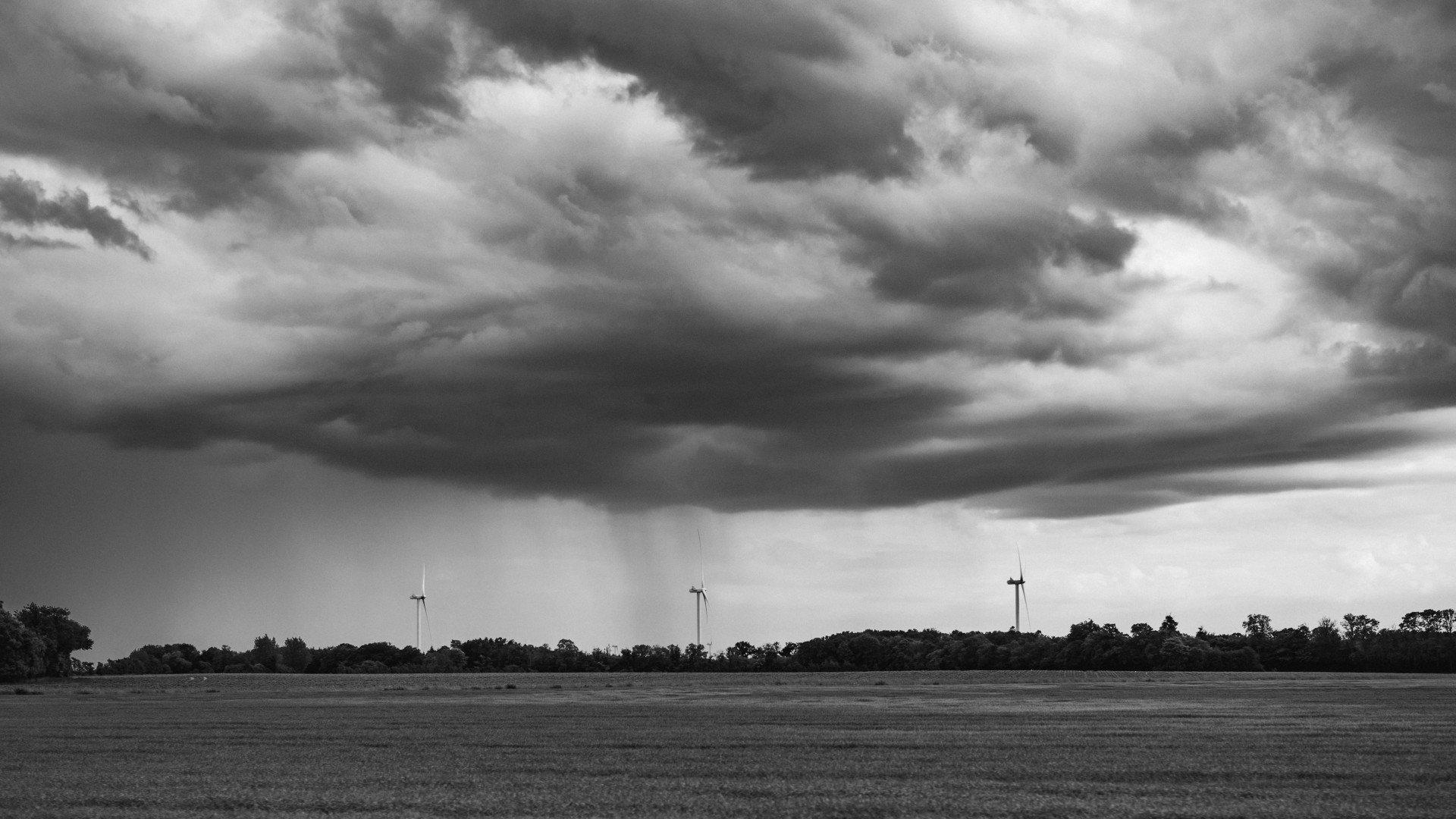 Black and white landscape with dramatic cloudy sky over rural field with wind turbines