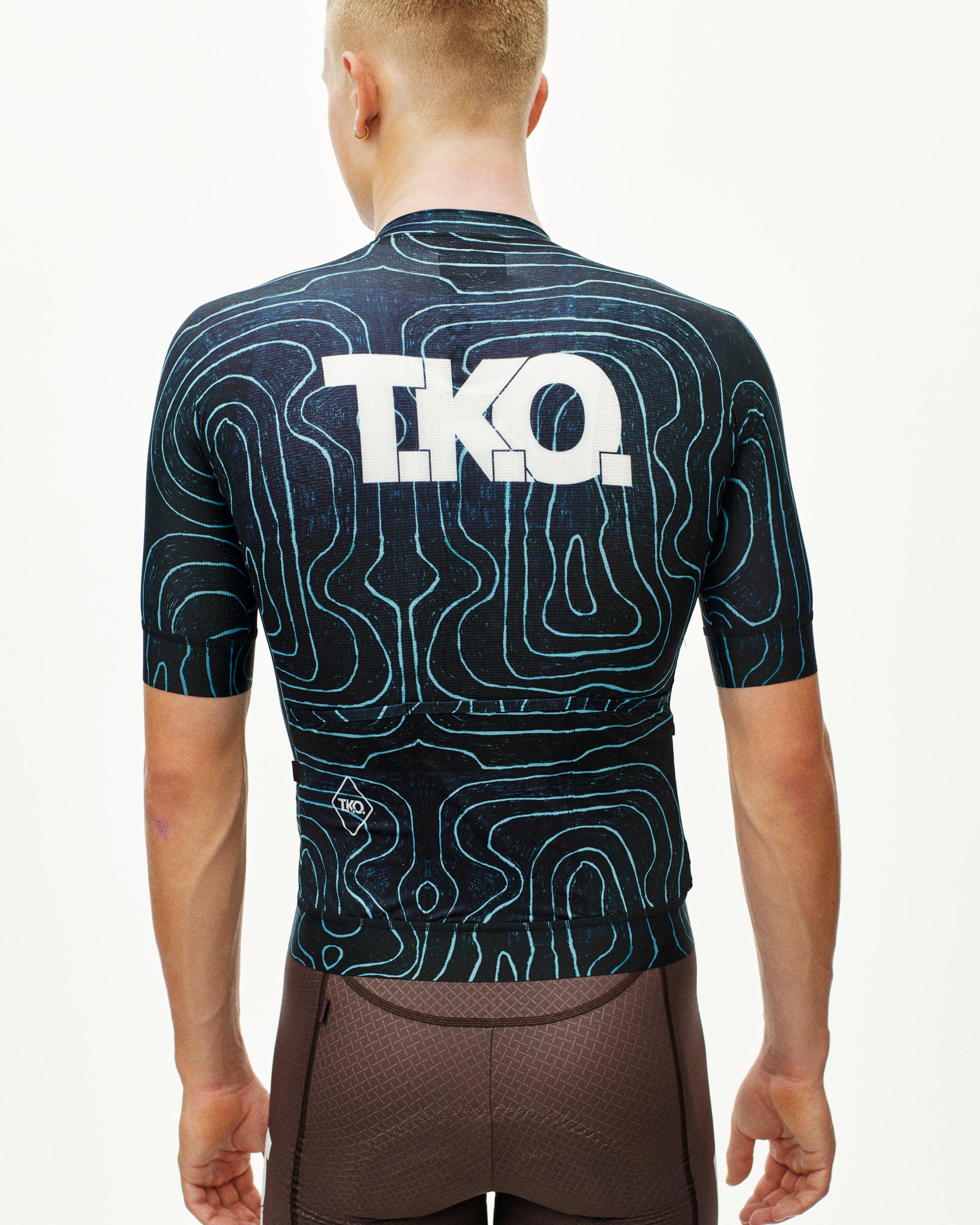 Blue T.K.O. Mechanism cycling jersey on model, rear view with topo map print and white chest logo