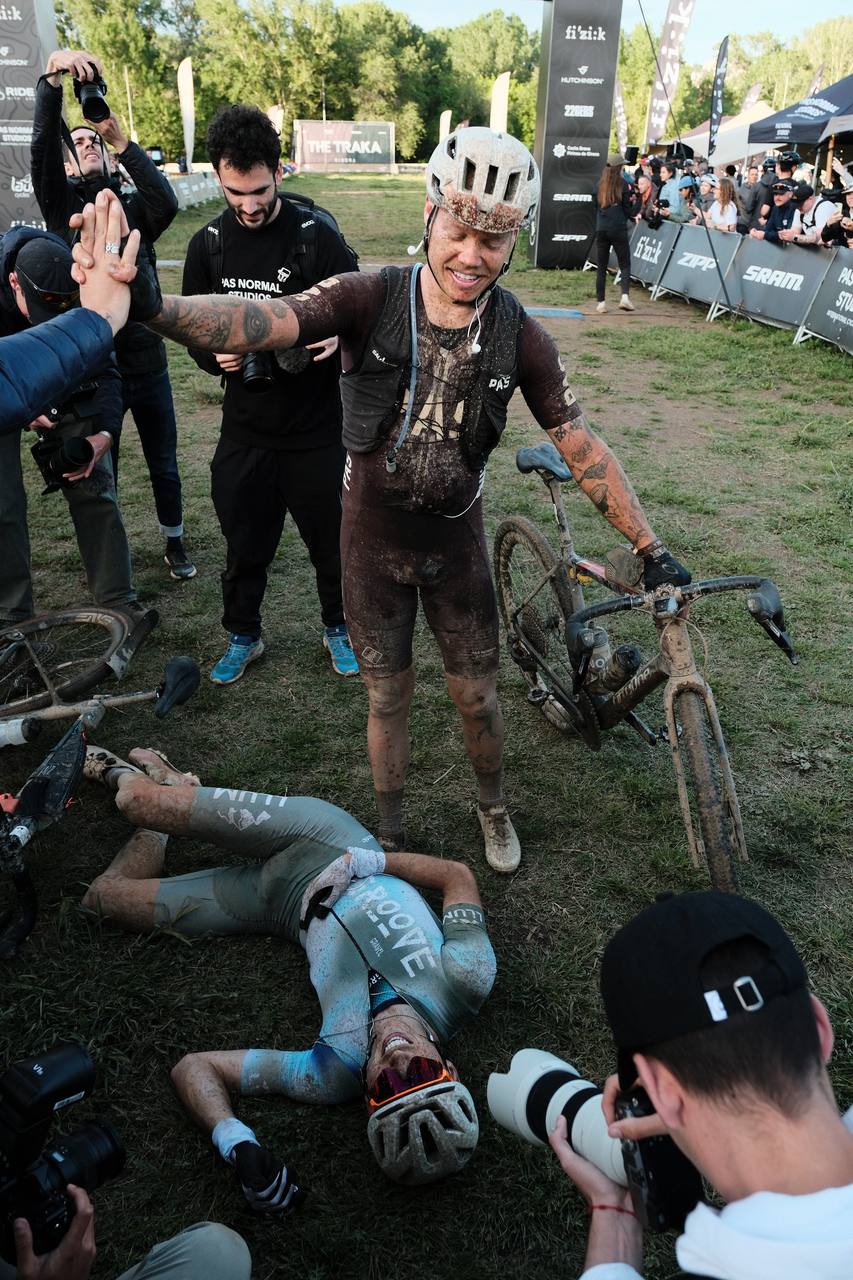 Cyclists celebrating after muddy gravel race finish, wearing PAS collection kit covered in dirt