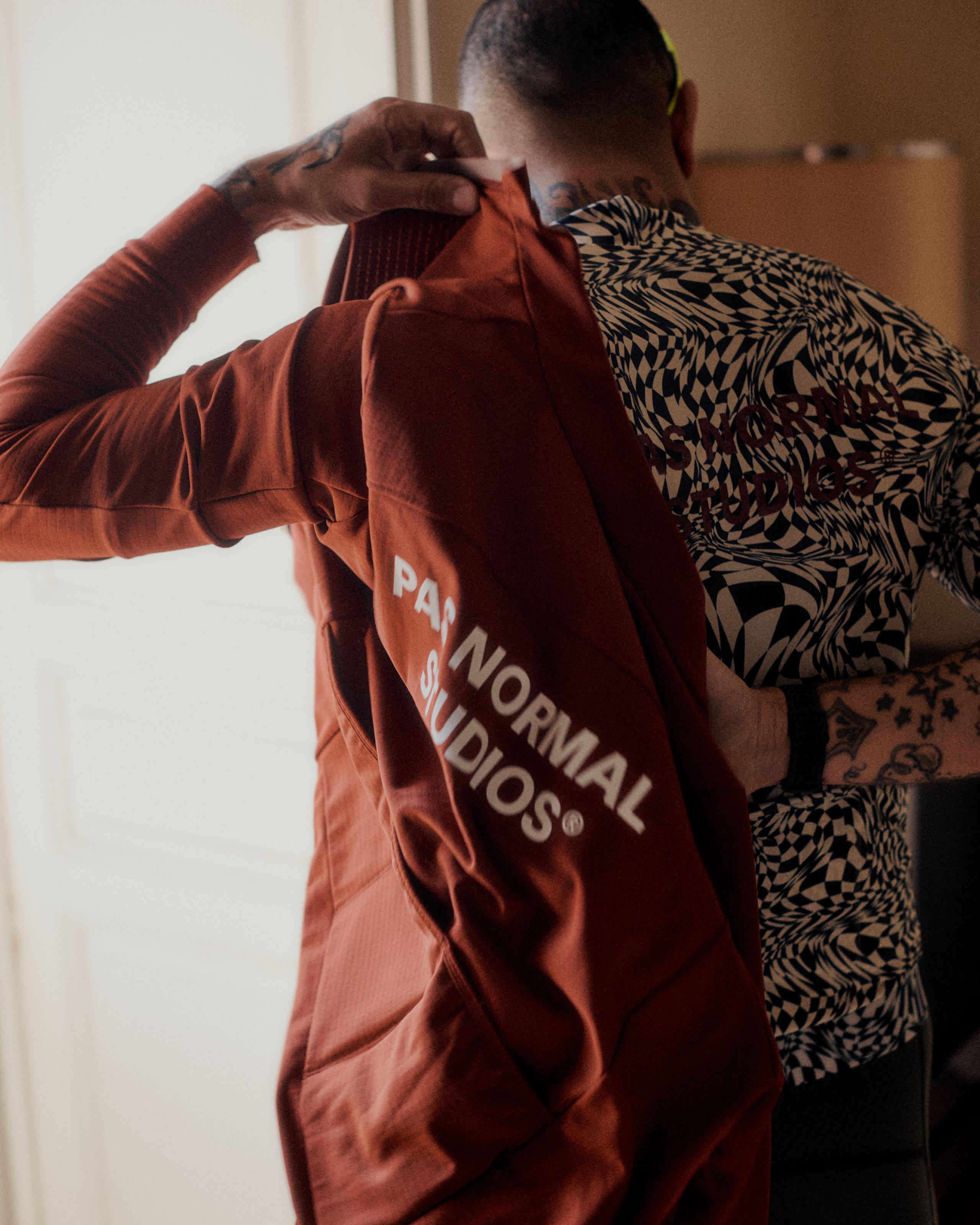 Model wearing black and white abstract patterned jersey holding rust colored garment with logo text