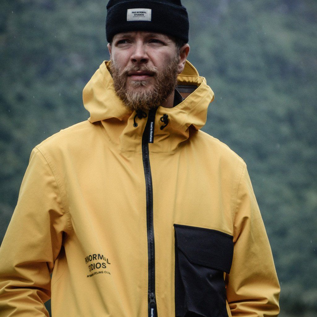 Model wearing yellow and navy rain jacket with hood and black beanie outdoors