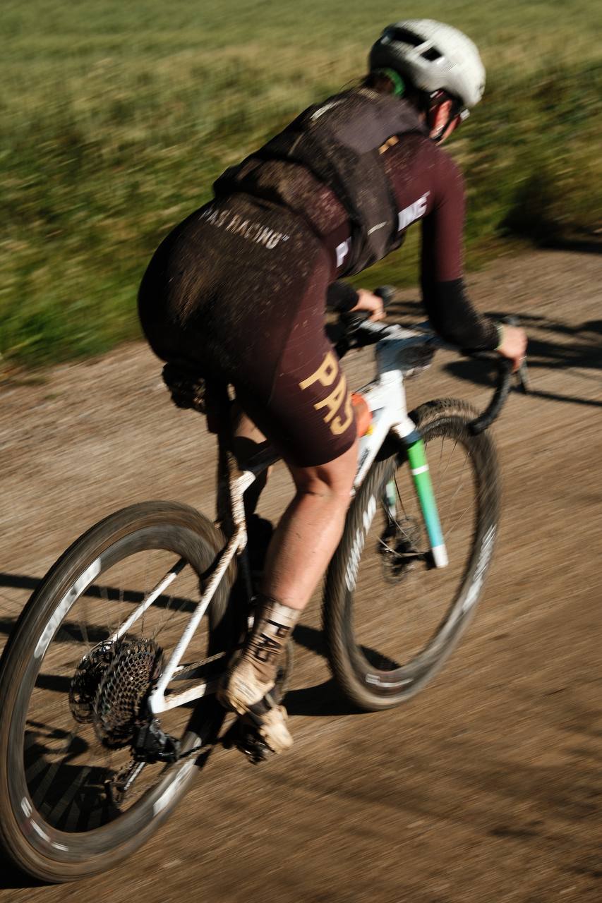 Cyclist in burgundy jersey and black shorts racing on gravel road in aerodynamic position
