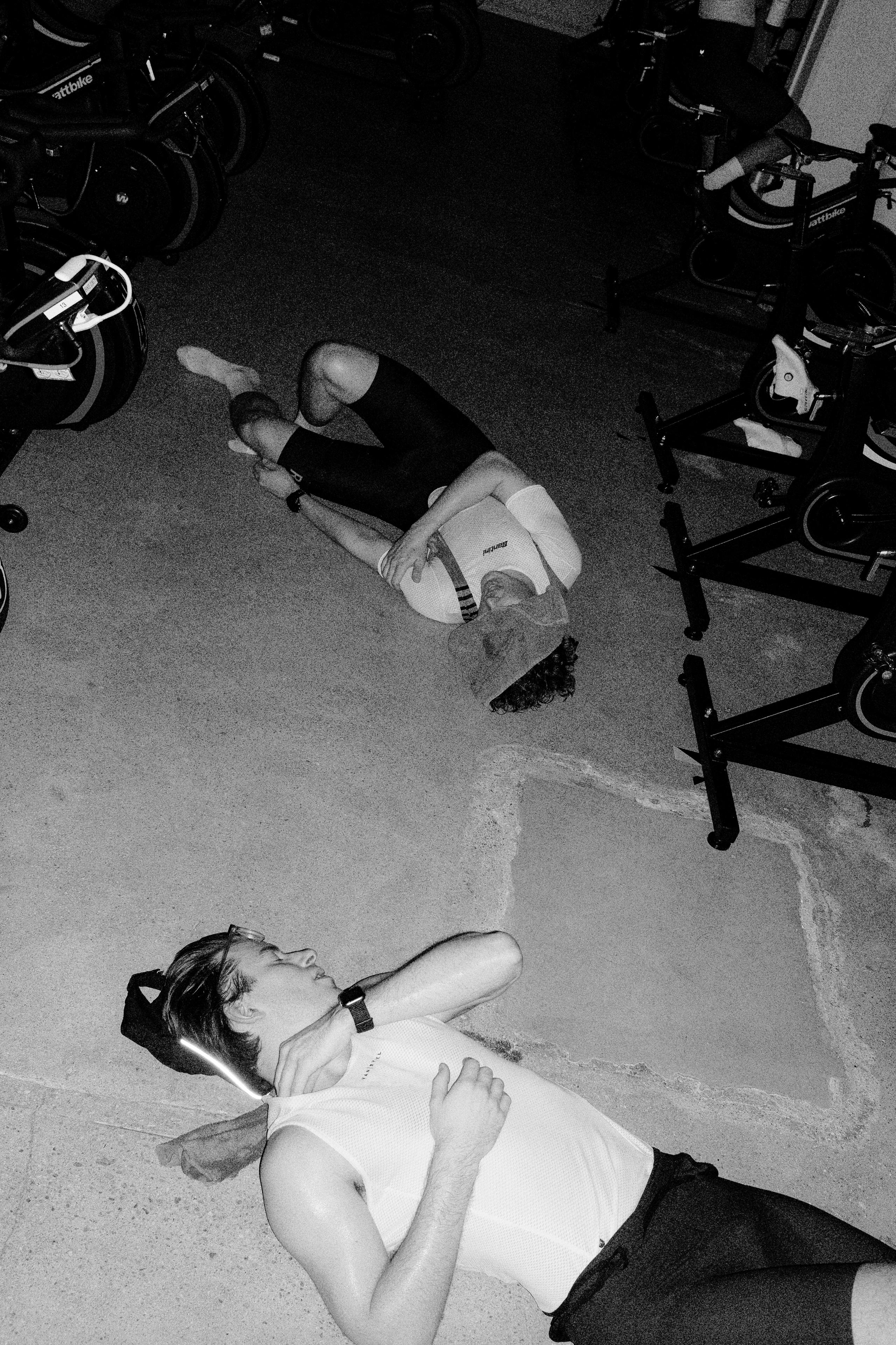 Models wearing cycling apparel resting on concrete floor surrounded by bikes after race