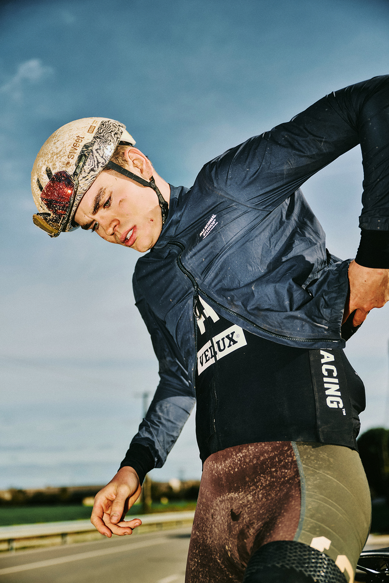 Model wearing navy wind jacket and black shorts with racing patches outdoors