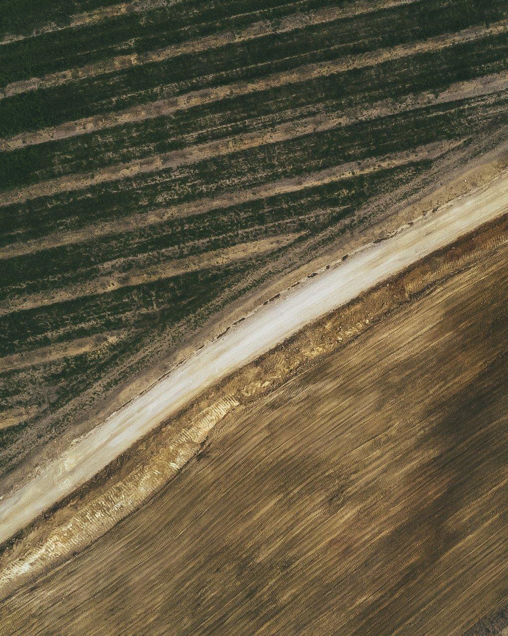 Aerial view of agricultural fields with dirt road cutting through striped farmland patterns