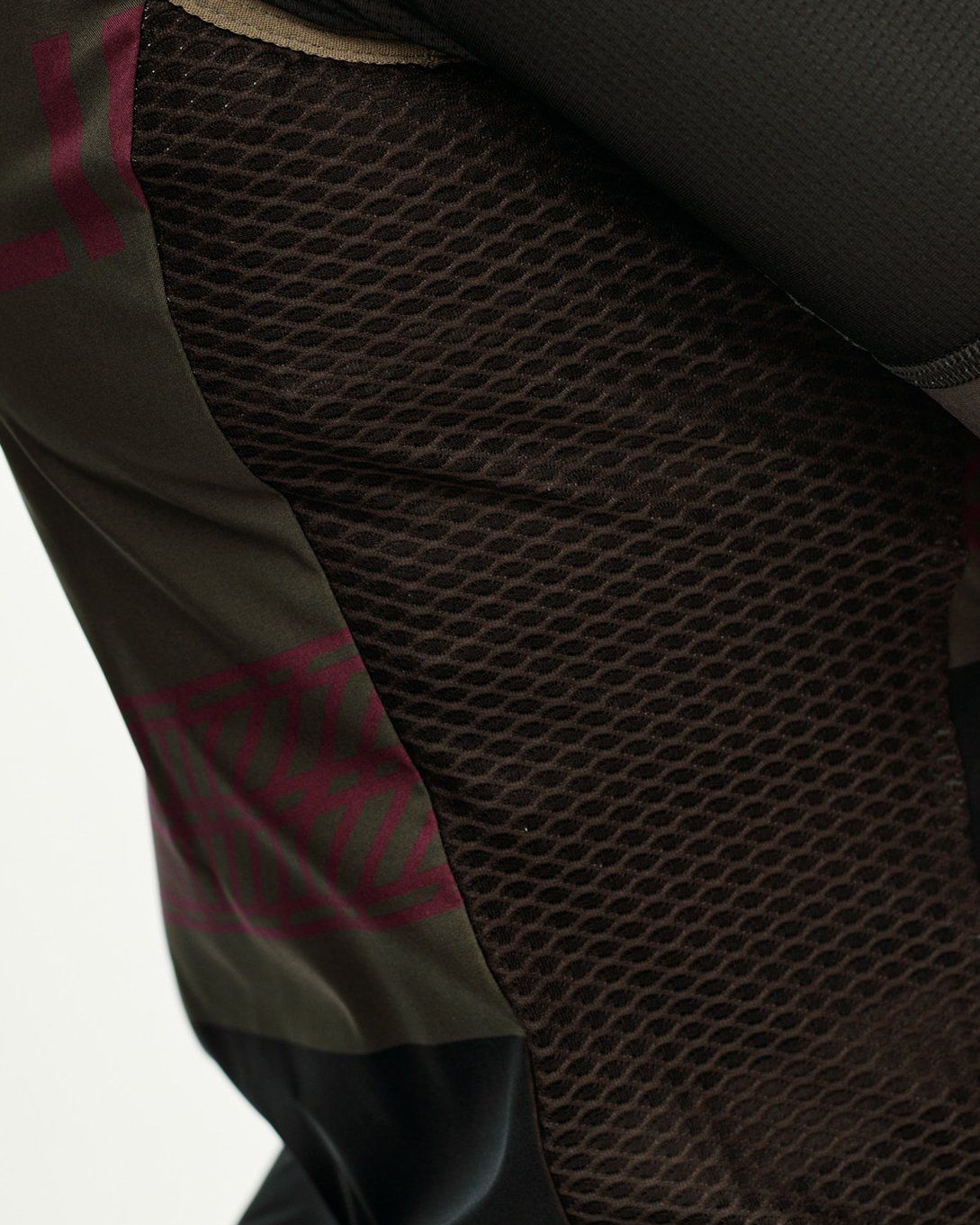 International Earth khaki Mechanism Stow Away cycling gilet, side detail on model with mesh panel and dark geometric print