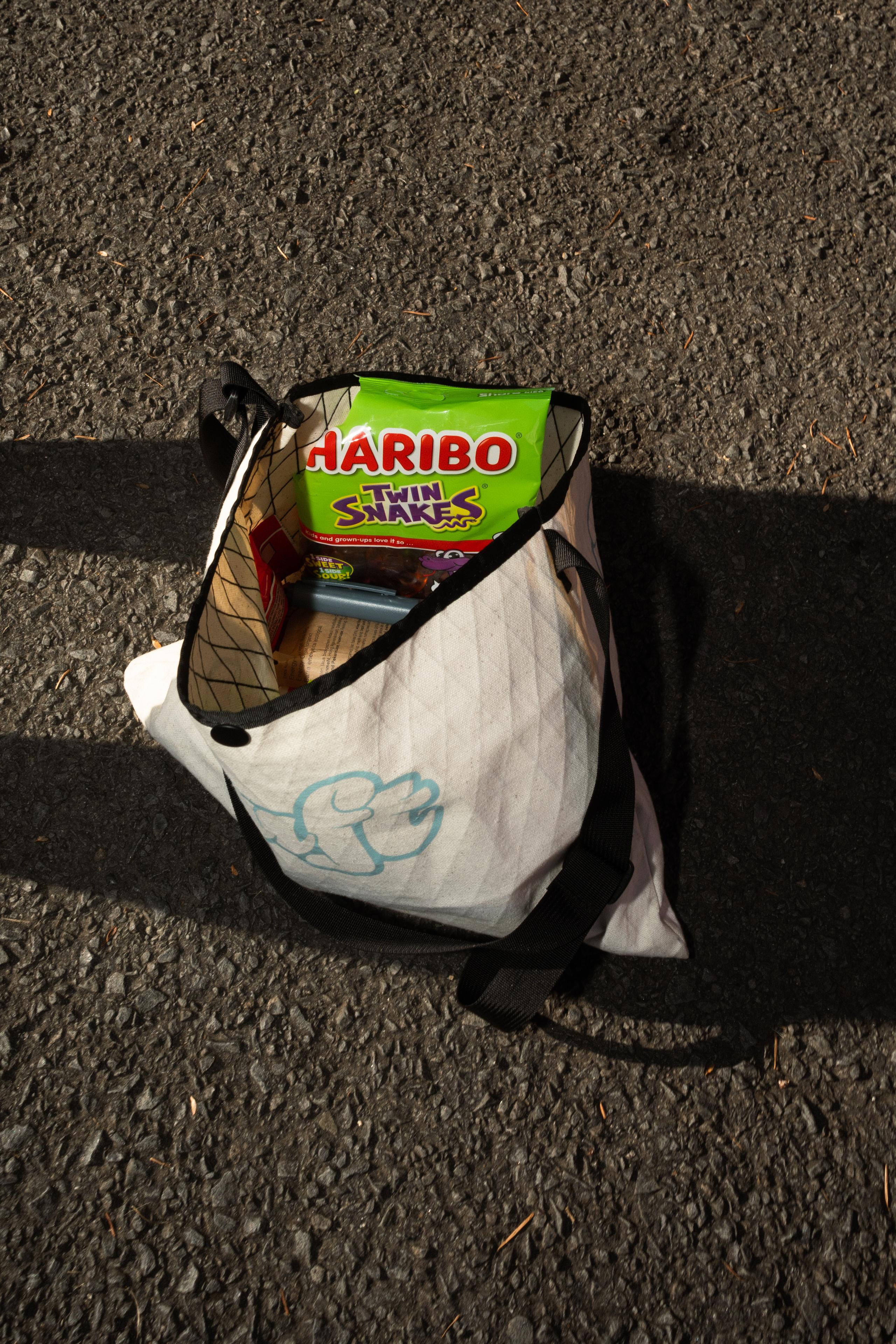White canvas bag with blue logo on asphalt containing cycling supplies and snacks