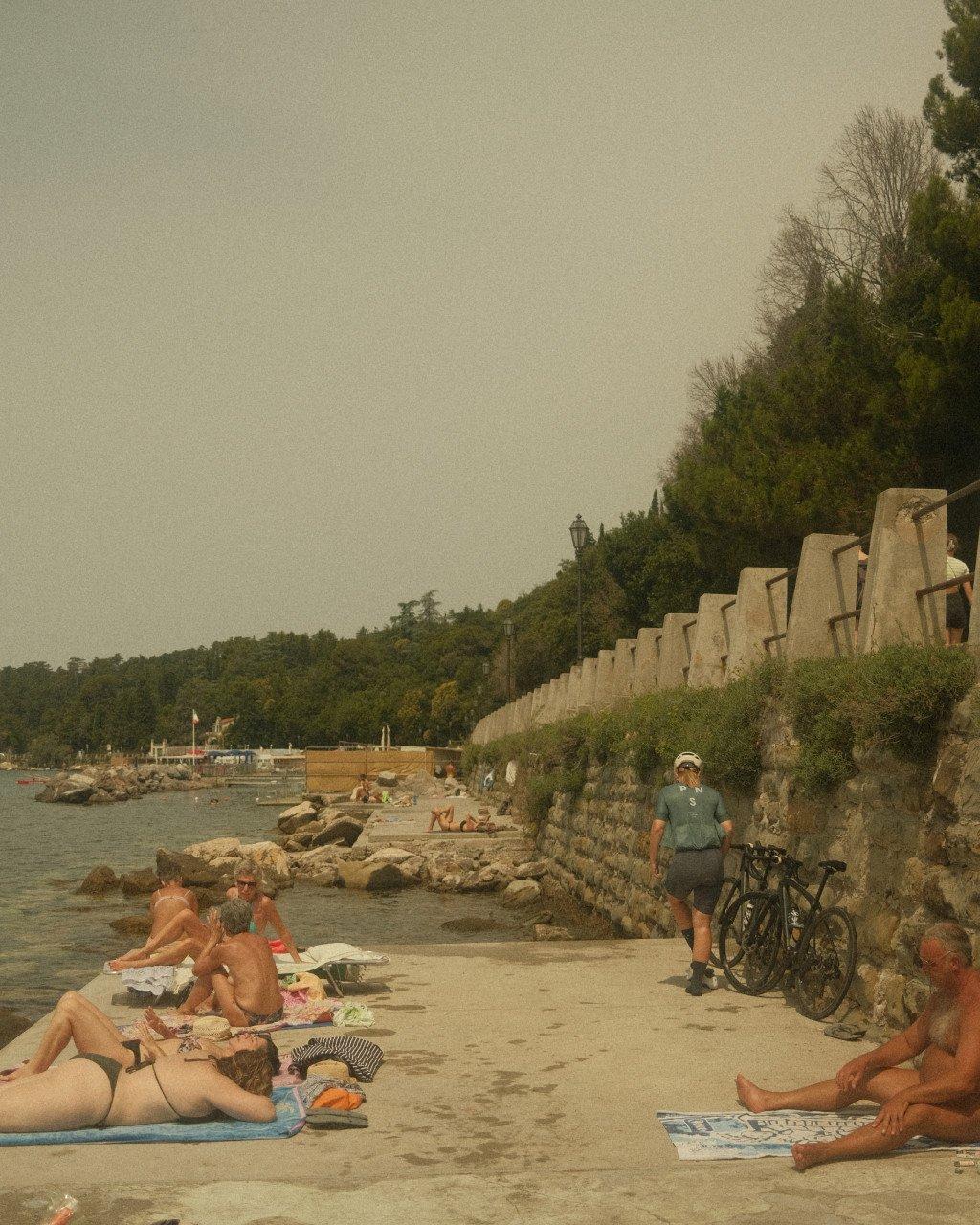Cyclist with road bike standing on coastal promenade near sunbathers on beach