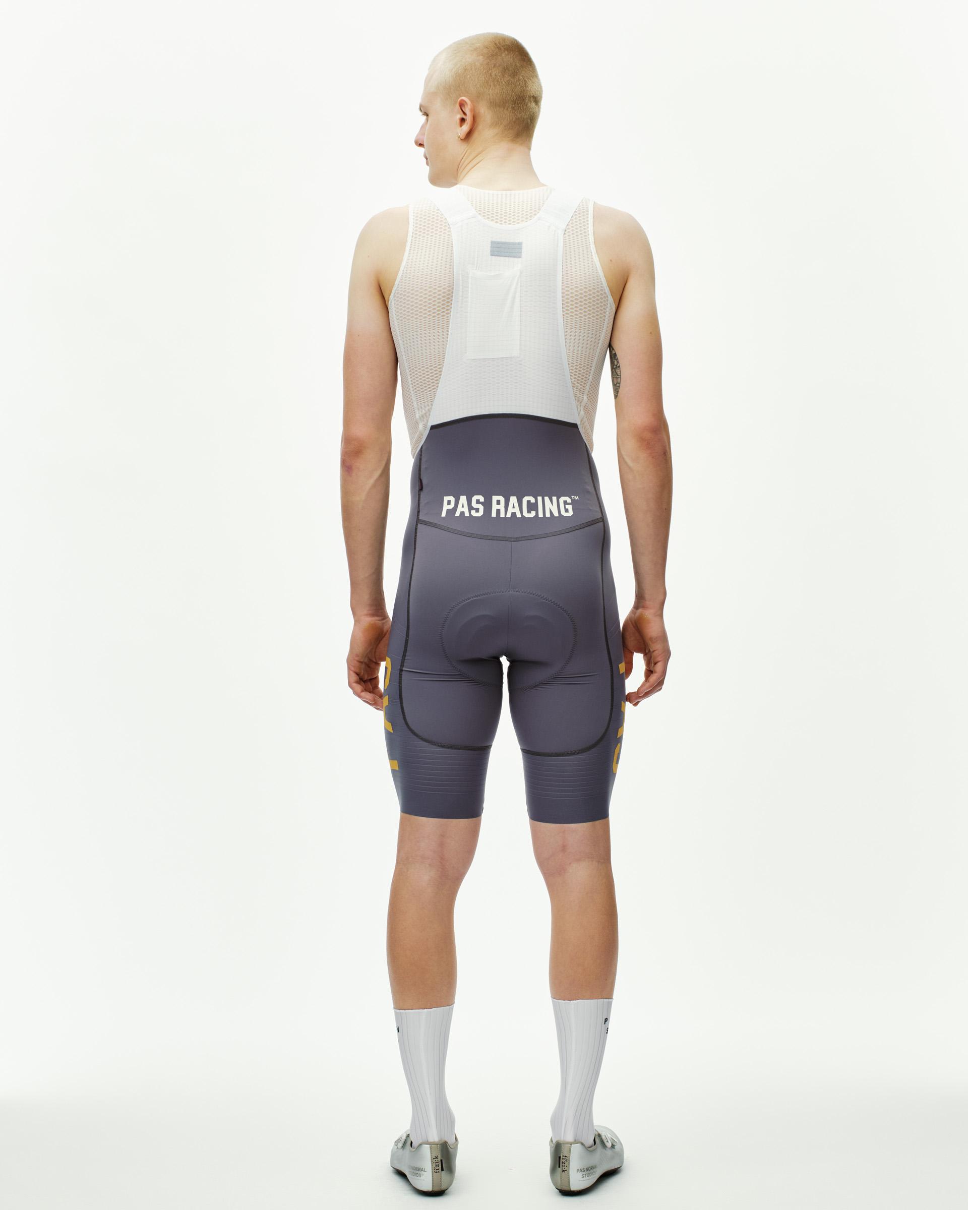 Grey PAS Mechanism Pro cycling bibs on model, rear view with white PAS Racing waistband print and gold side panels