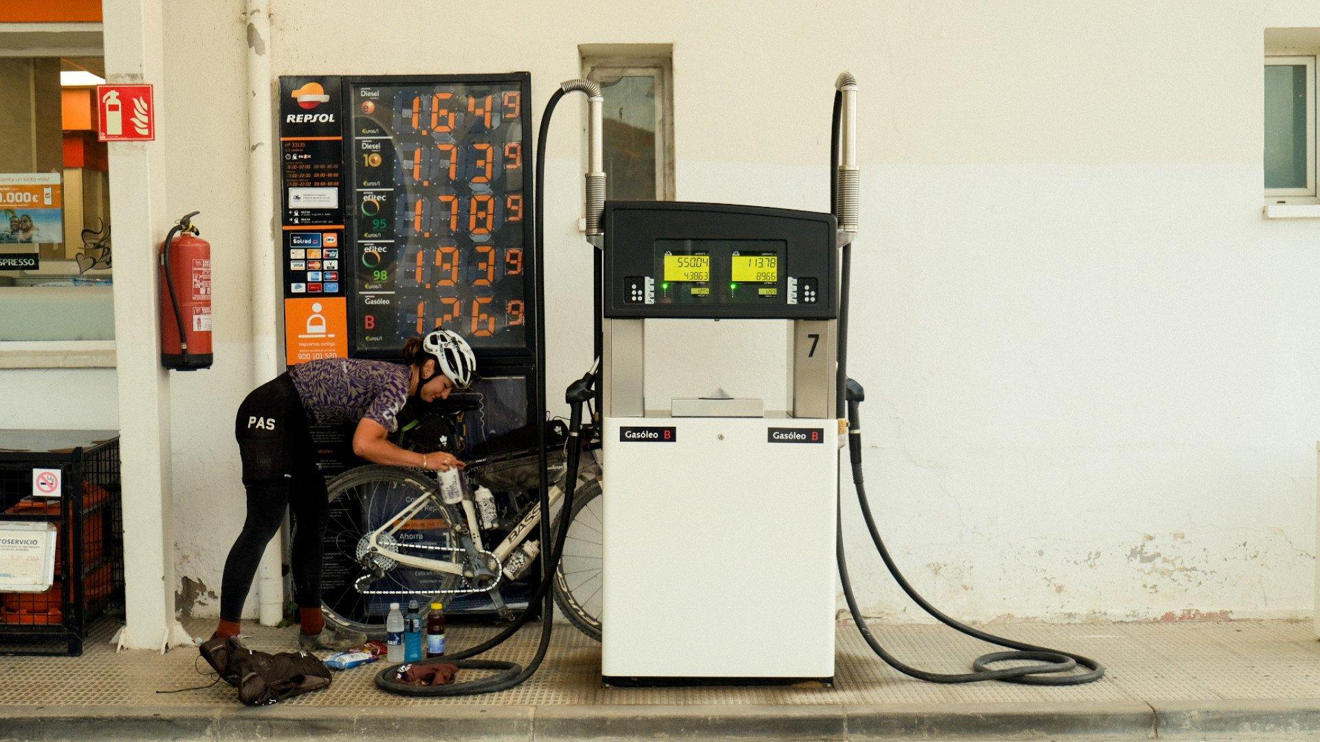 Model wearing PAS collection jersey and tights maintaining bicycle at gas station