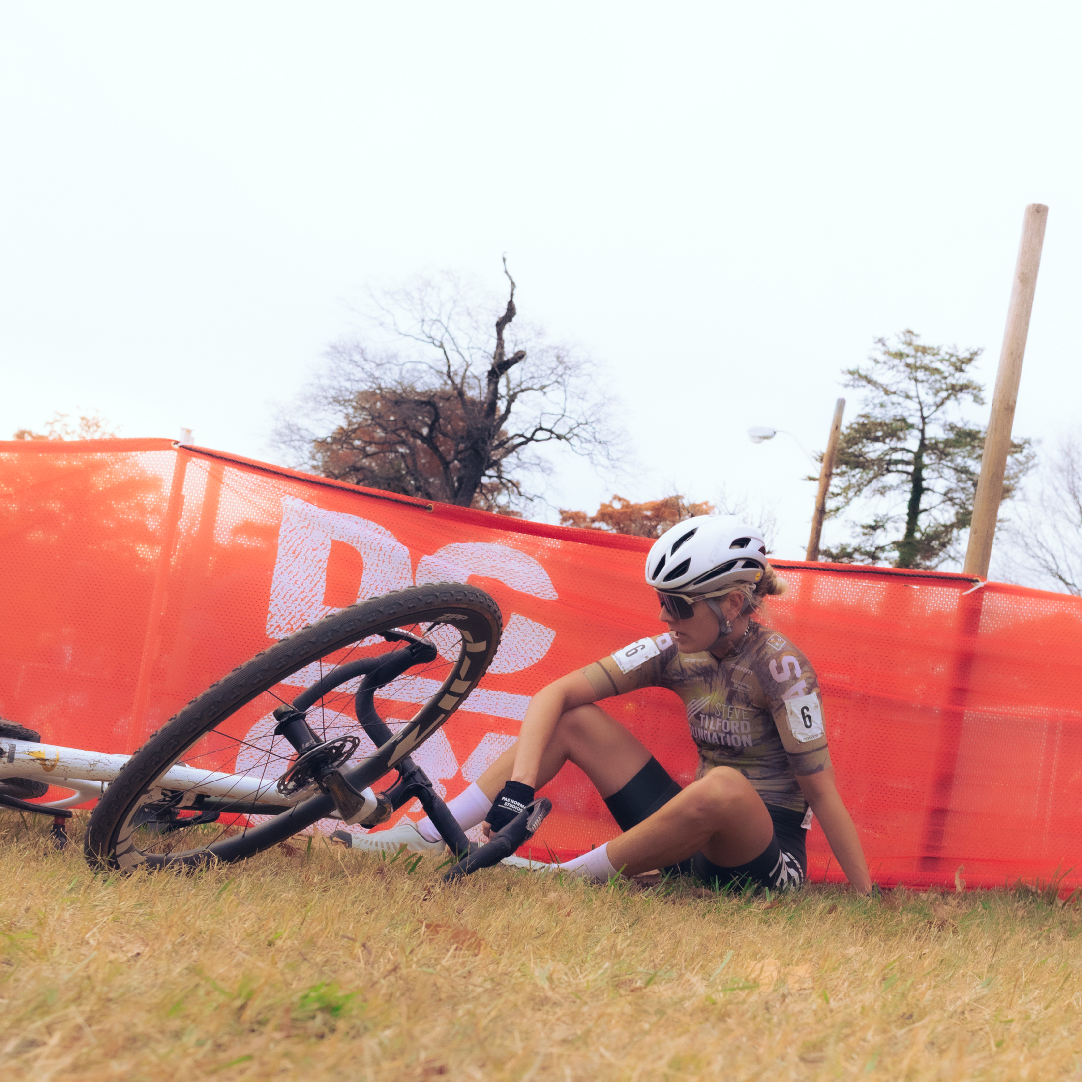 Female cyclist in brown jersey resting beside bike during cyclocross race