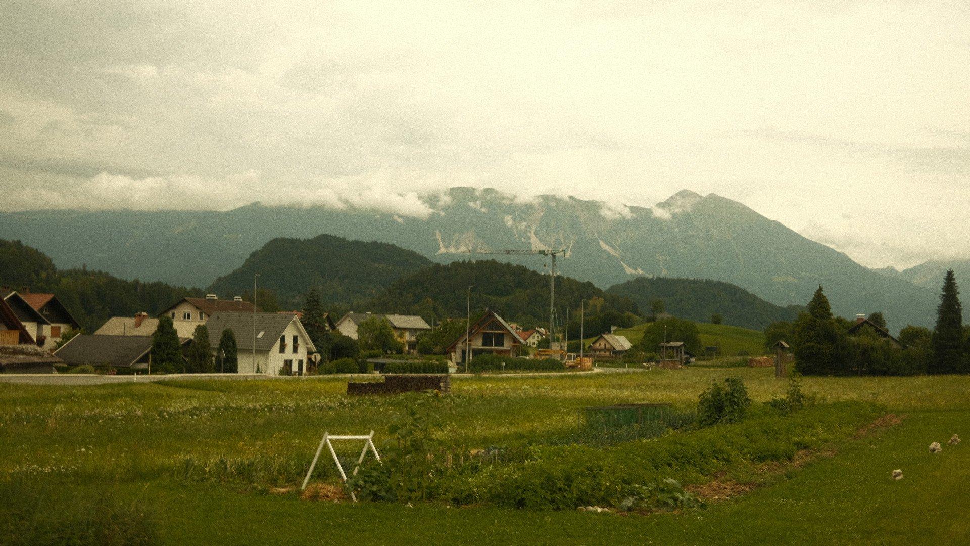 Alpine village with houses and fields beneath cloudy mountain peaks in Slovenia
