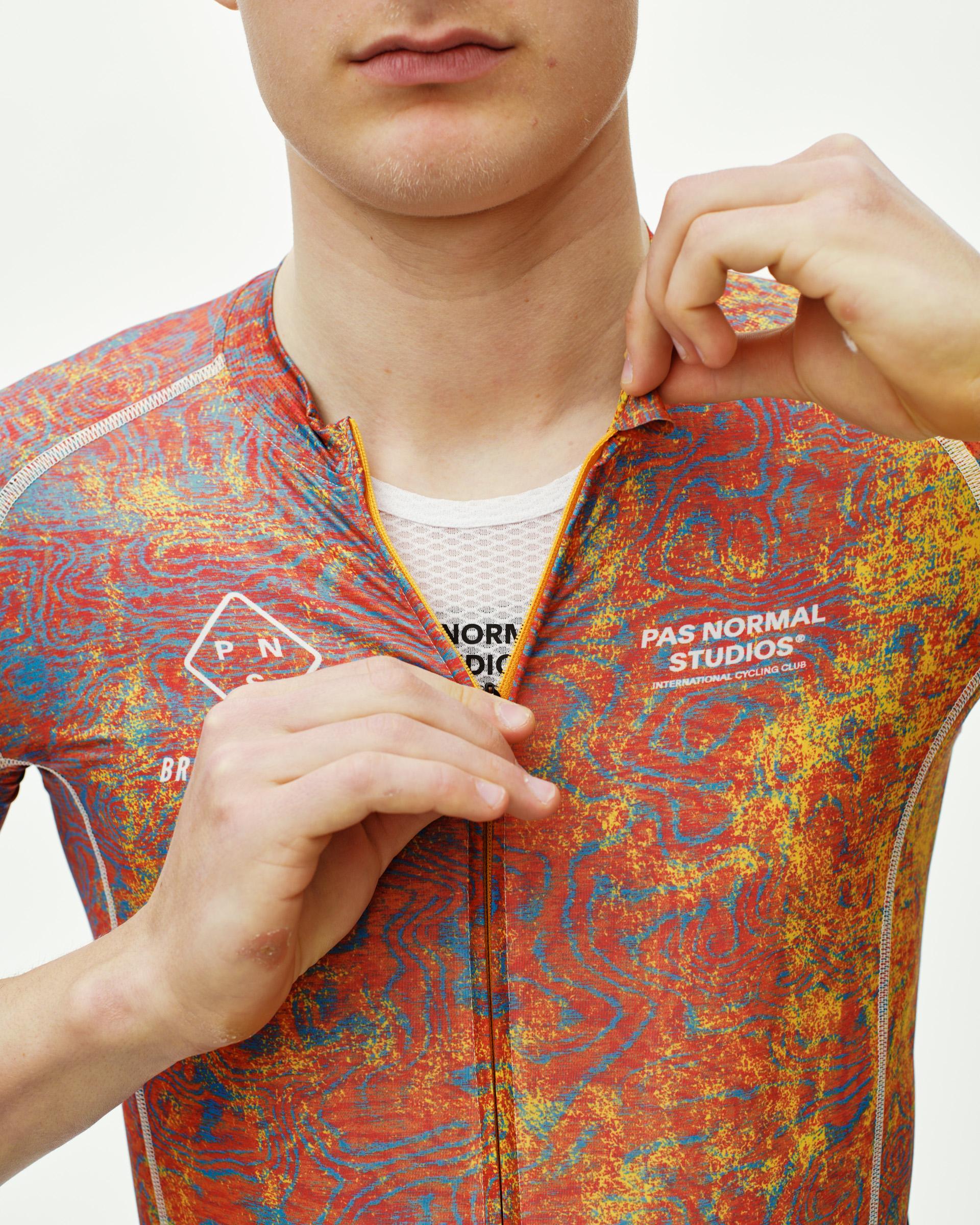 Red-orange Mechanism Breakfast Club cycling jersey front detail on model with allover topographic print and chest logo