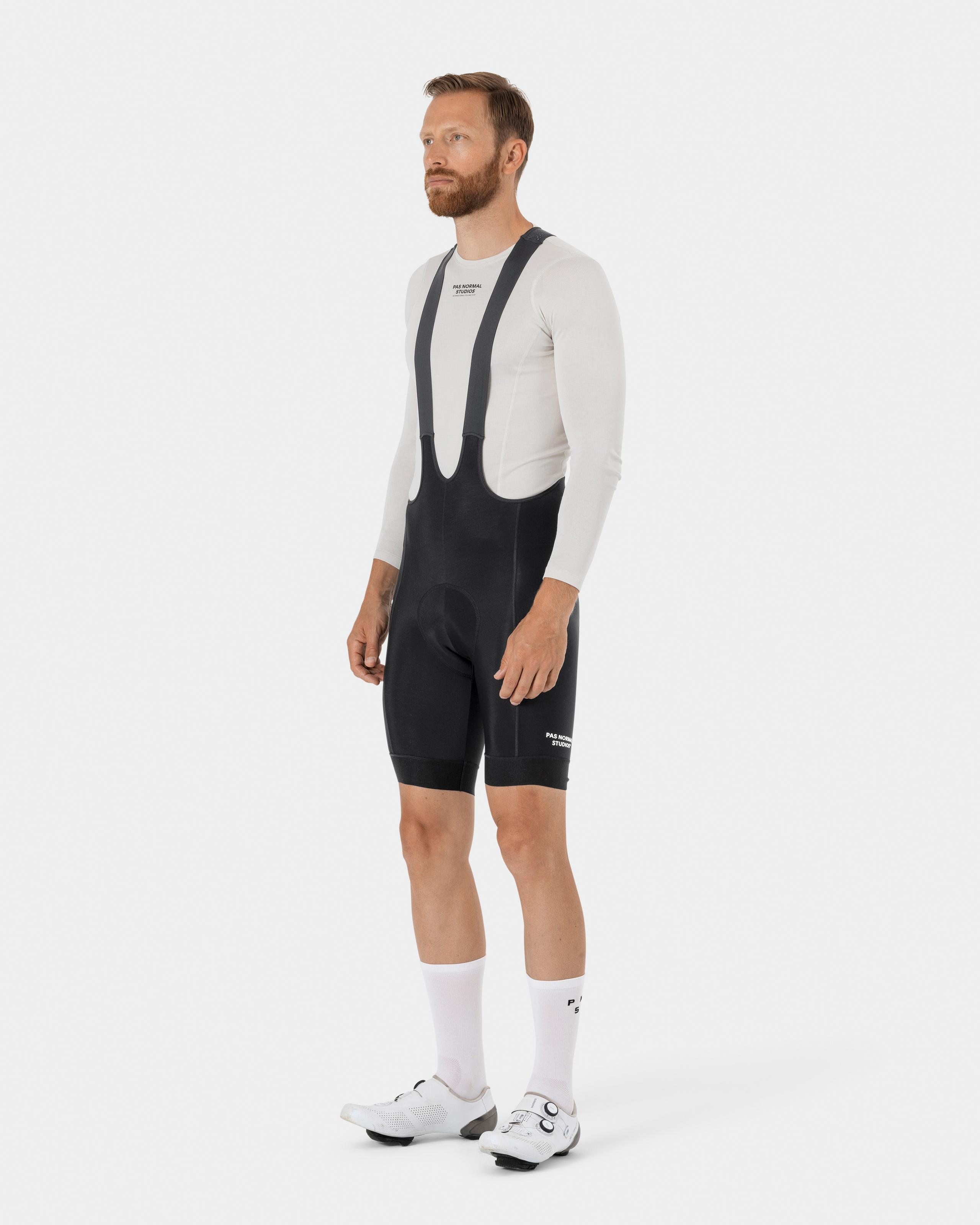 Black Essential Thermal cycling bibs on model, three-quarter view with white long sleeve jersey