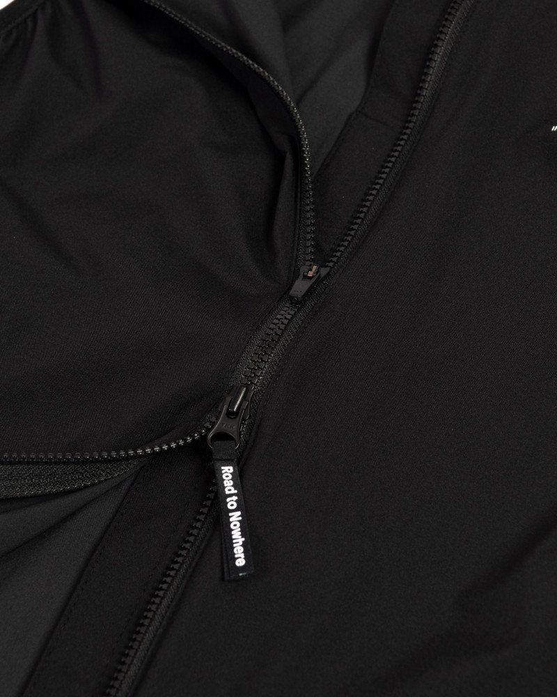 Black Mechanism Stow Away gilet, detail view showing zip pull with white branded tag