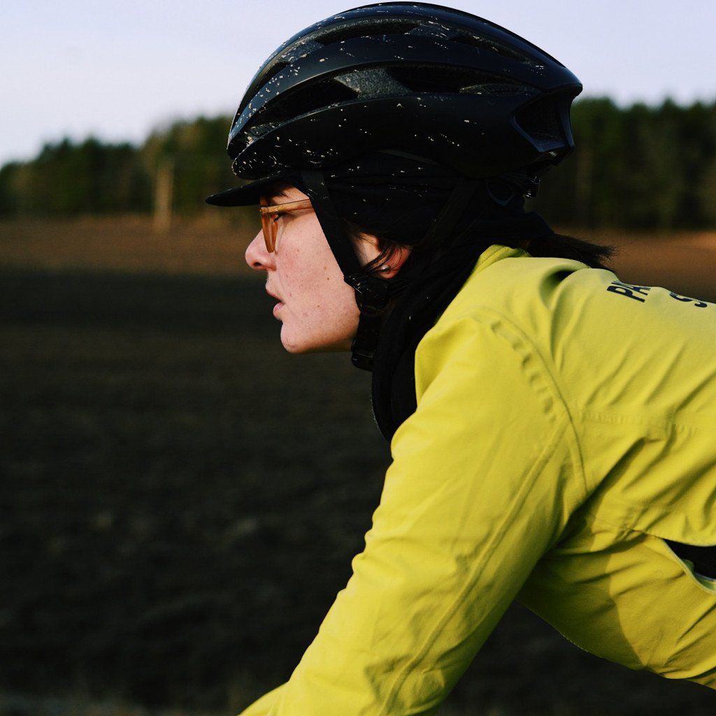 Model wearing yellow cycling jacket and black helmet in countryside setting