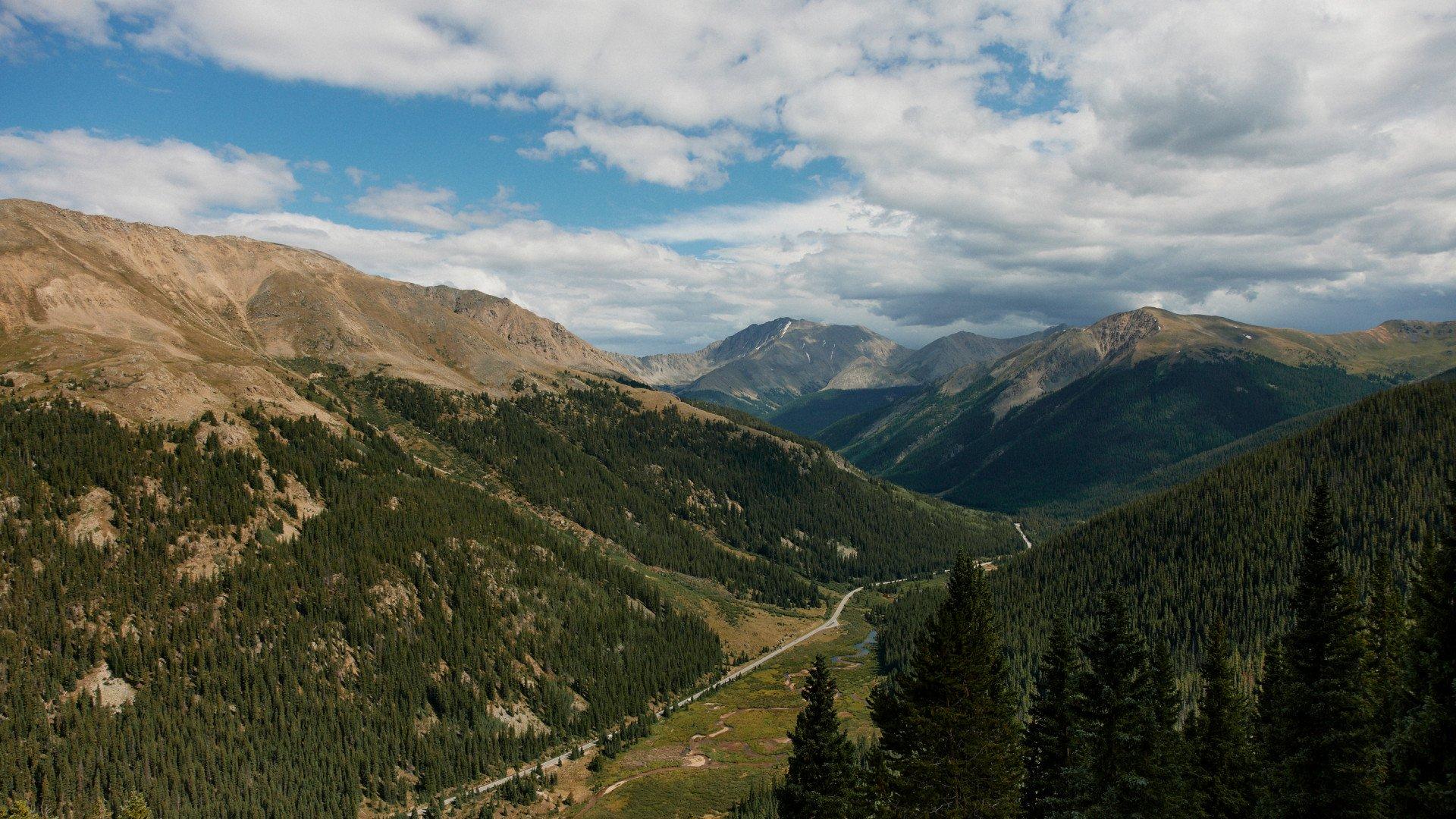Mountain landscape with winding road through forested valley under cloudy sky