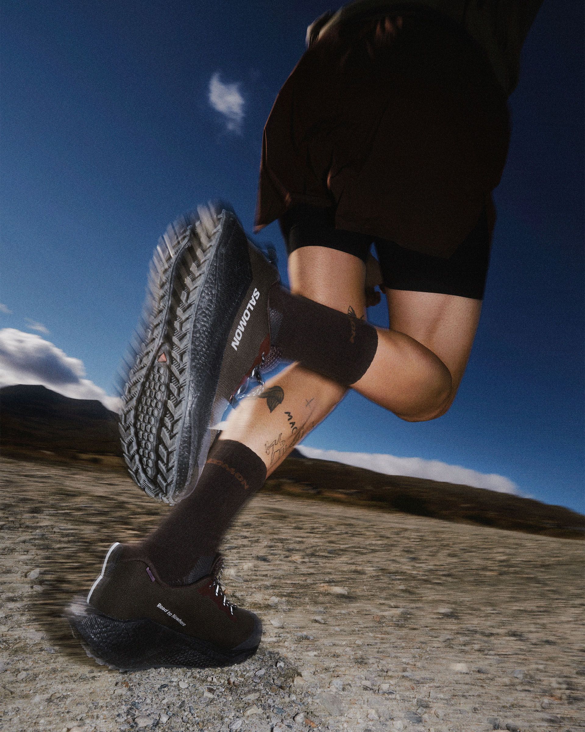 Light Brown Salomon AERO BLAZE 4 GRVL GTX trail shoe on model running on gravel, sole view showing lugged outsole