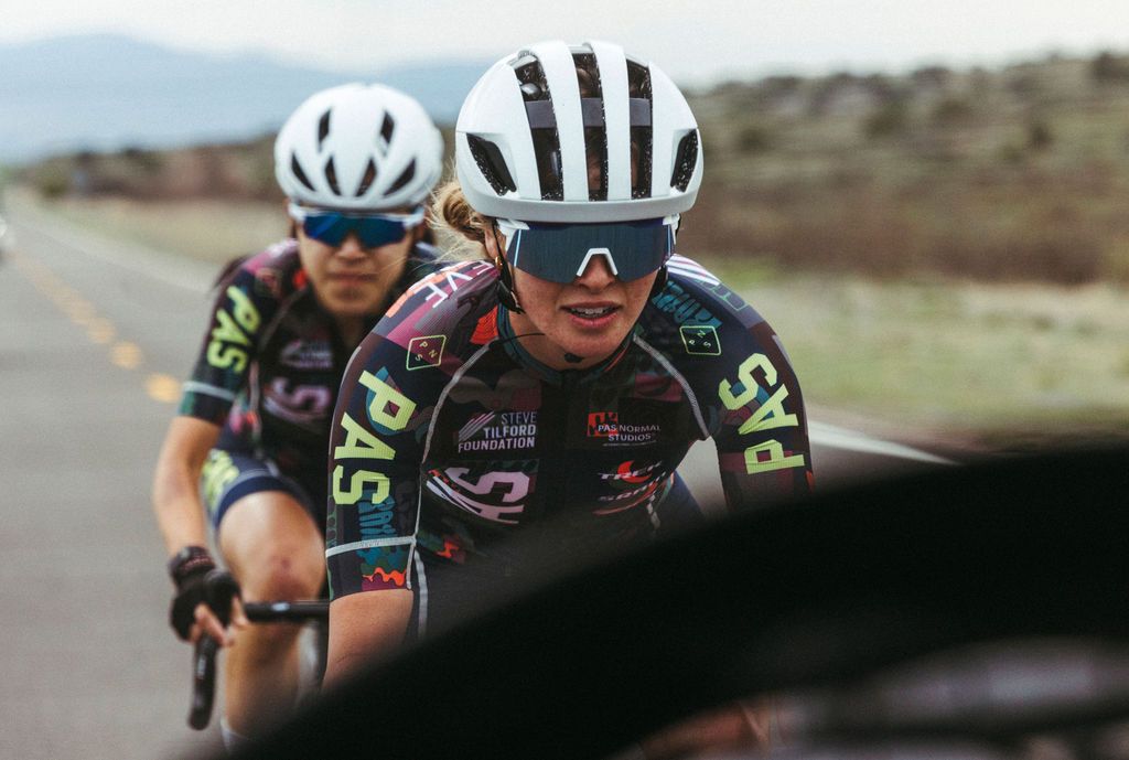 Two cyclists in aerodynamic position wearing colorful cycling kit with sponsor logos during road race