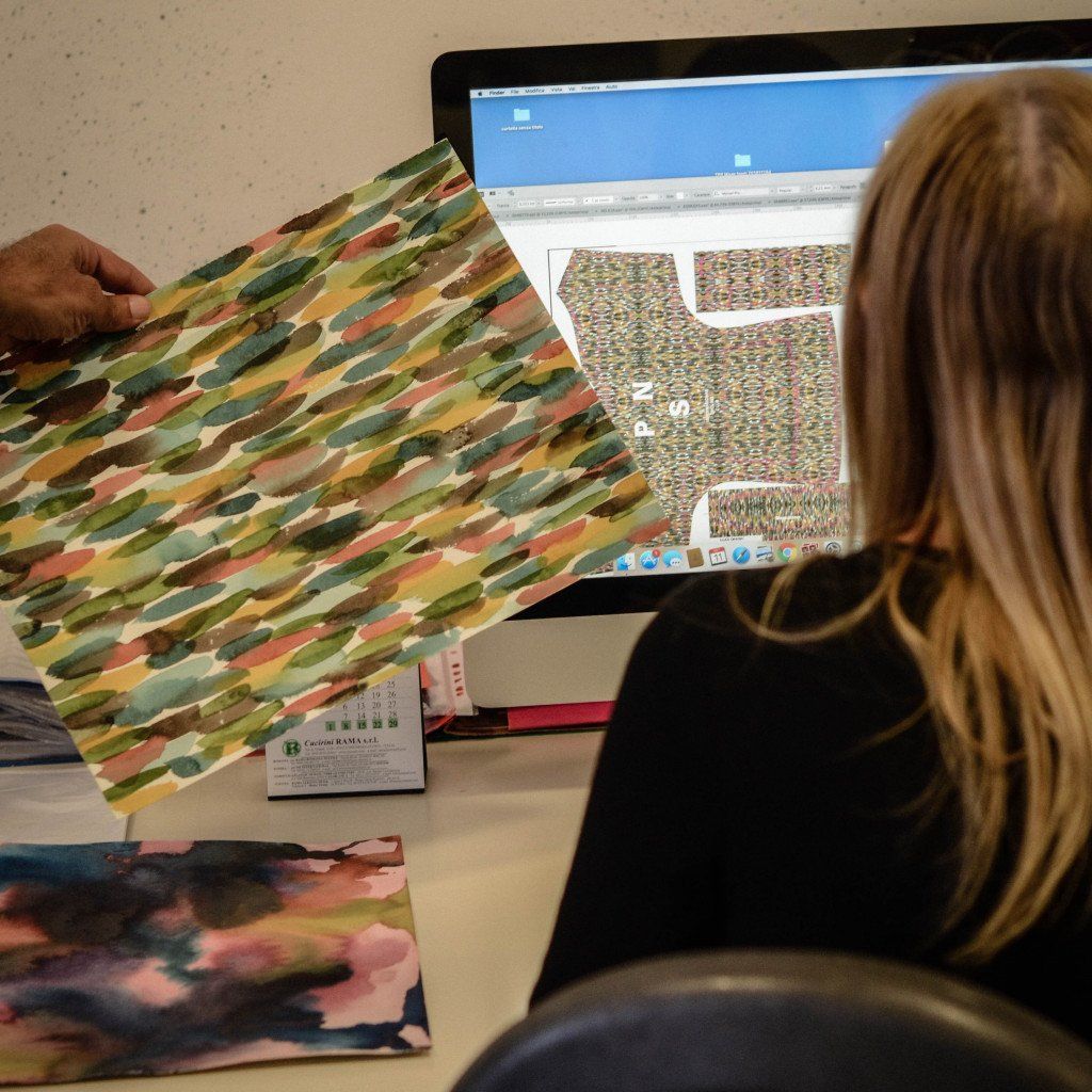 Designer reviewing colorful fabric samples and digital patterns on computer screen for cycling apparel development