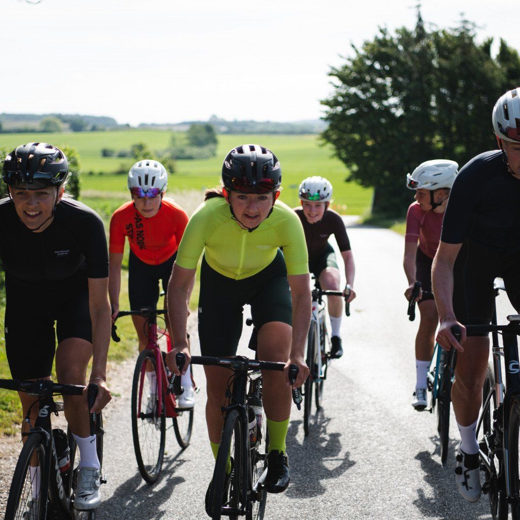 Cyclists in racing position on country road wearing various colorful cycling apparel including green and red jerseys