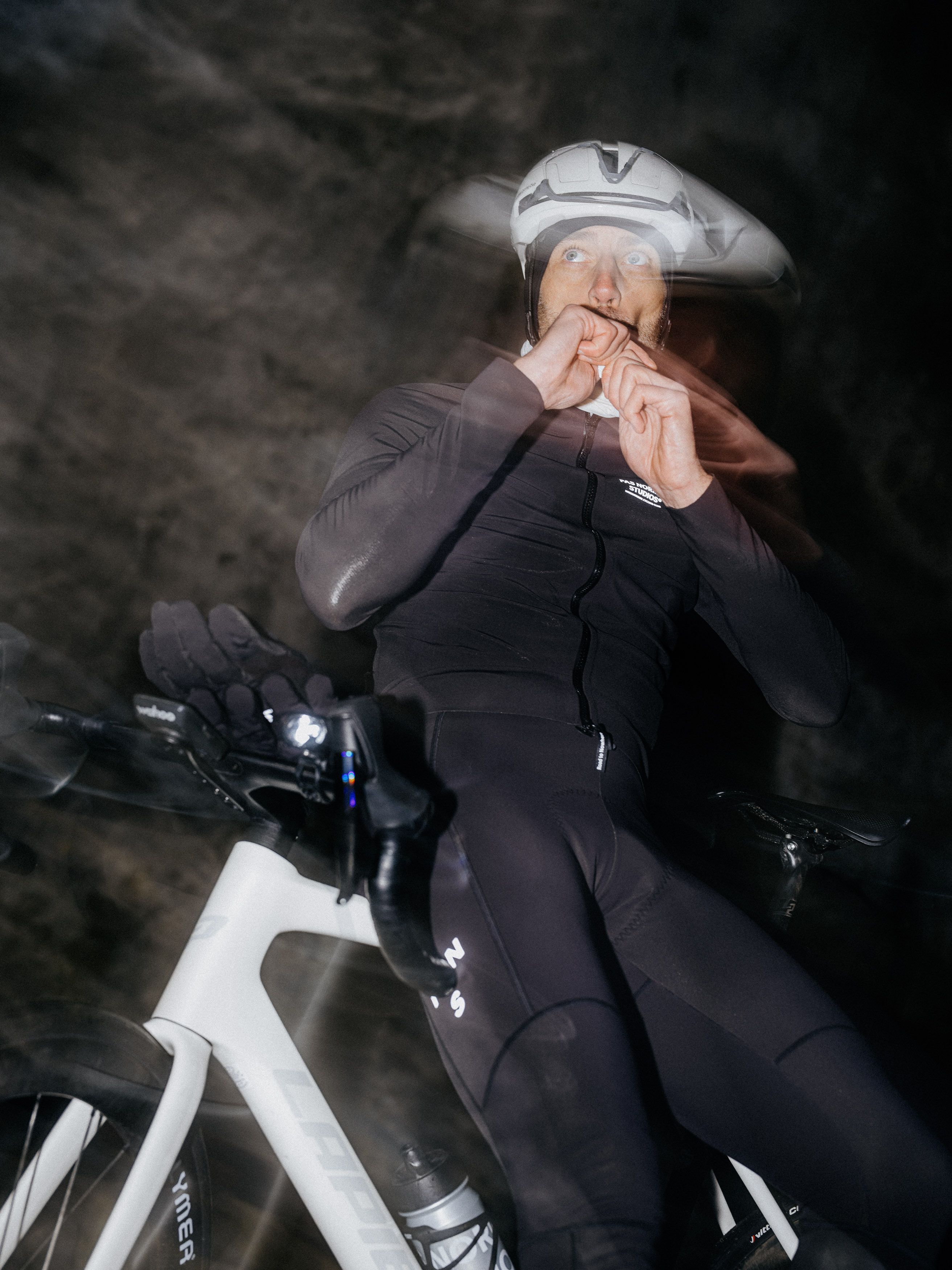 Model wearing dark cycling kit with white helmet on bike in tunnel or cave setting
