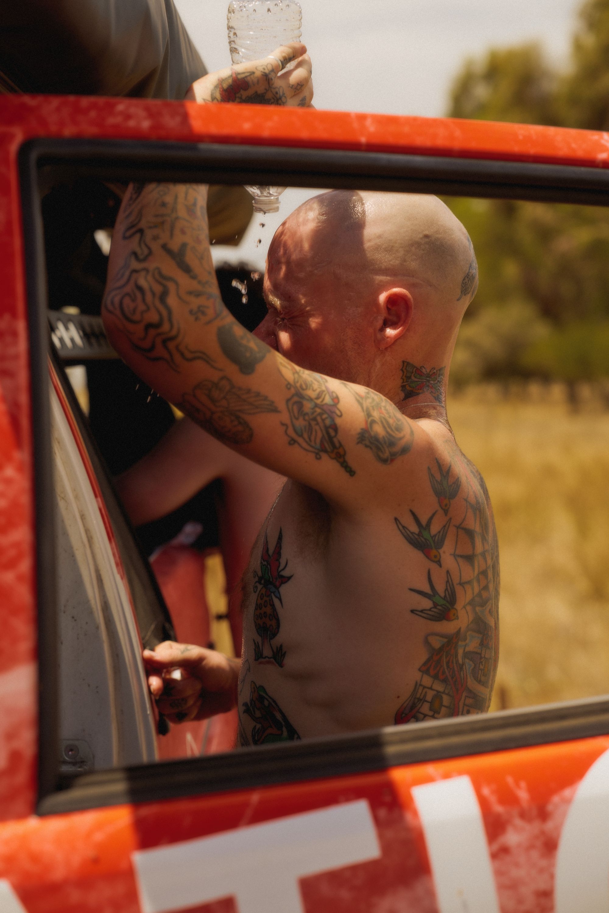 Tattooed man in red vehicle holding water bottle outdoors