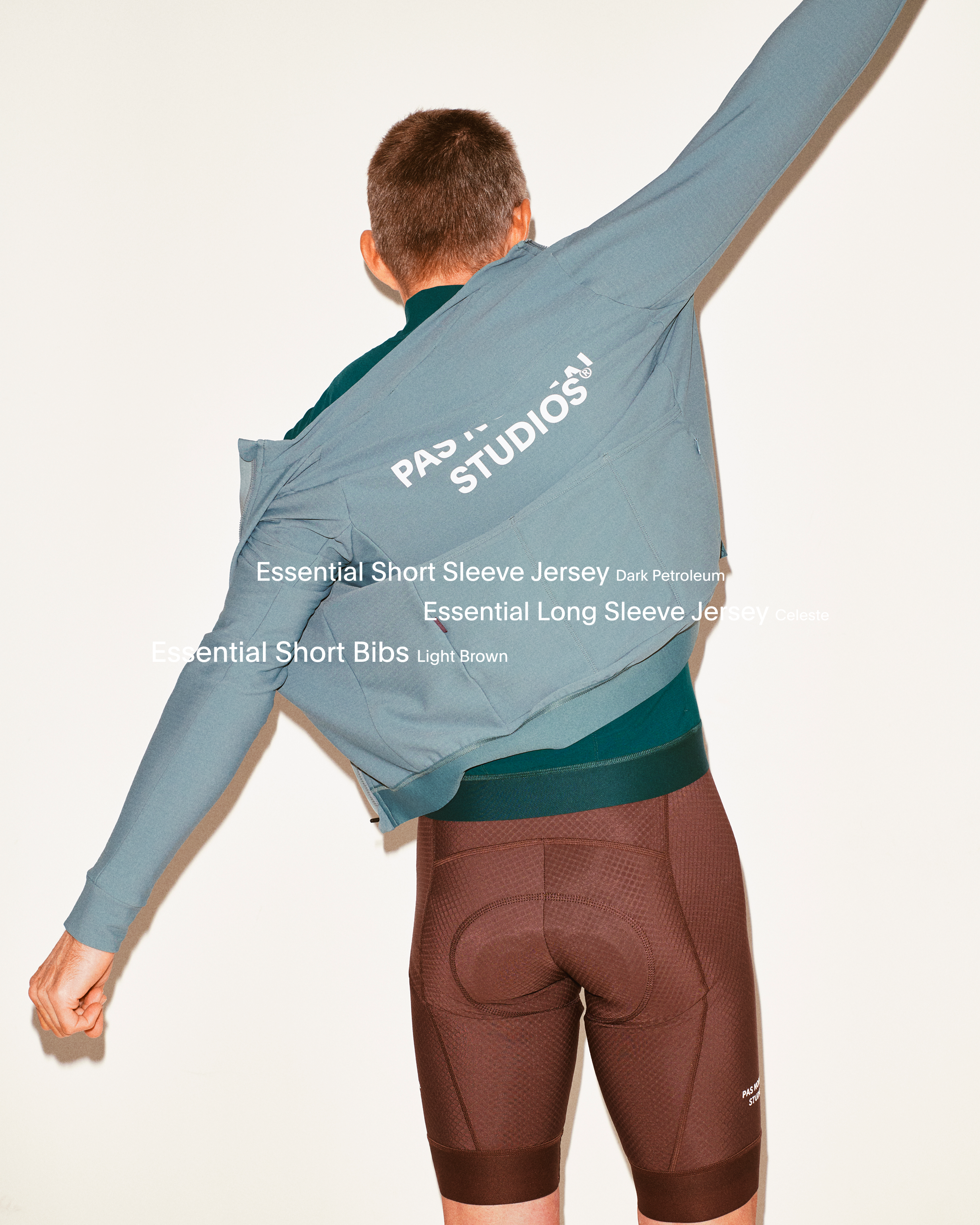 Model wearing Men's Essential Short Sleeve Jersey in grey with green base layer and brown bibs, back view in studio