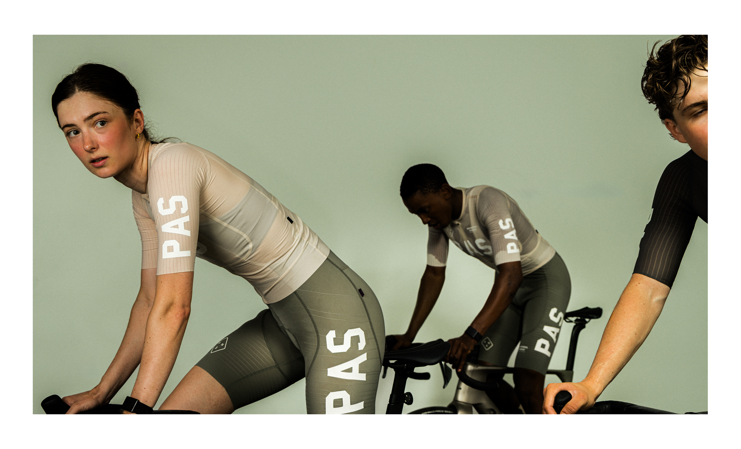 Models wearing beige cycling apparel with white lettering in aerodynamic position on indoor trainers